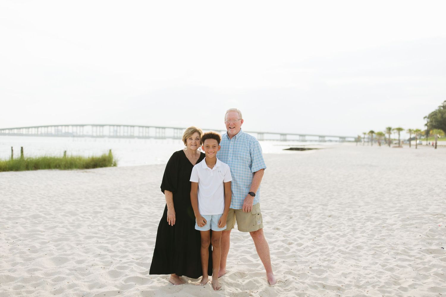 Family members pose for casual photos during their beach photoshoot on a bright sandy shore.