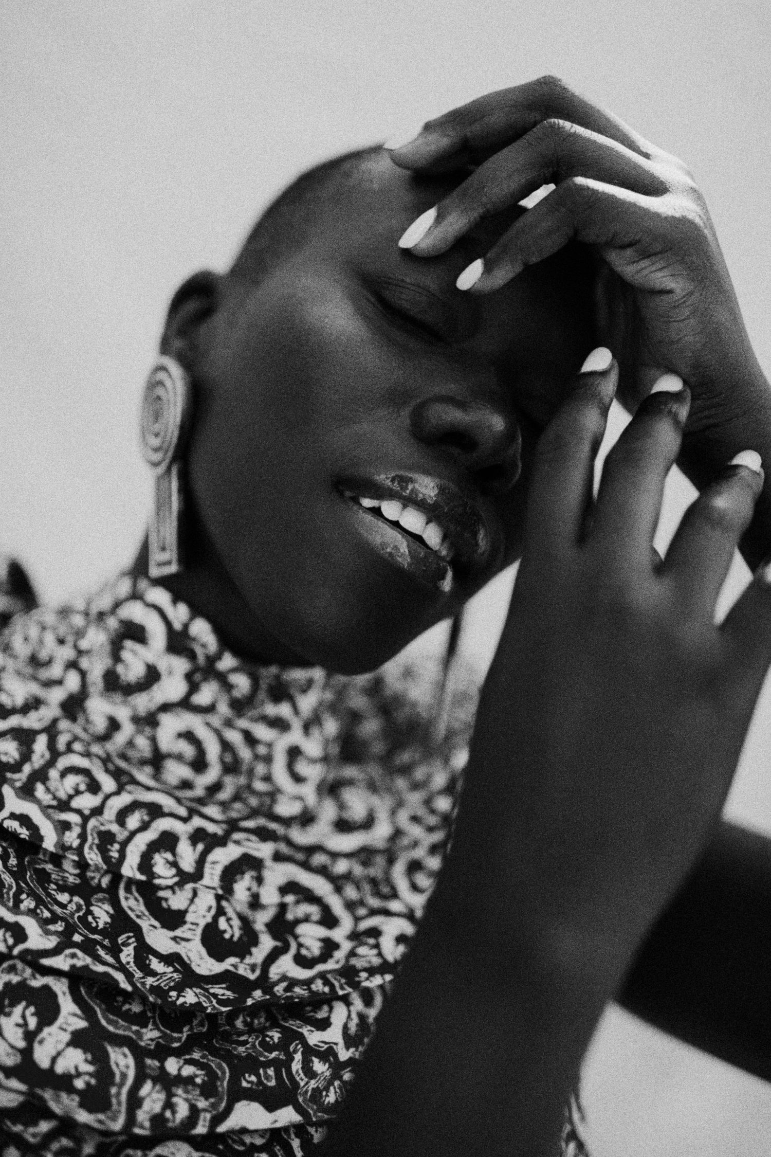 A black and white artistic portrait shows hands touching a figure against a patterned backdrop.