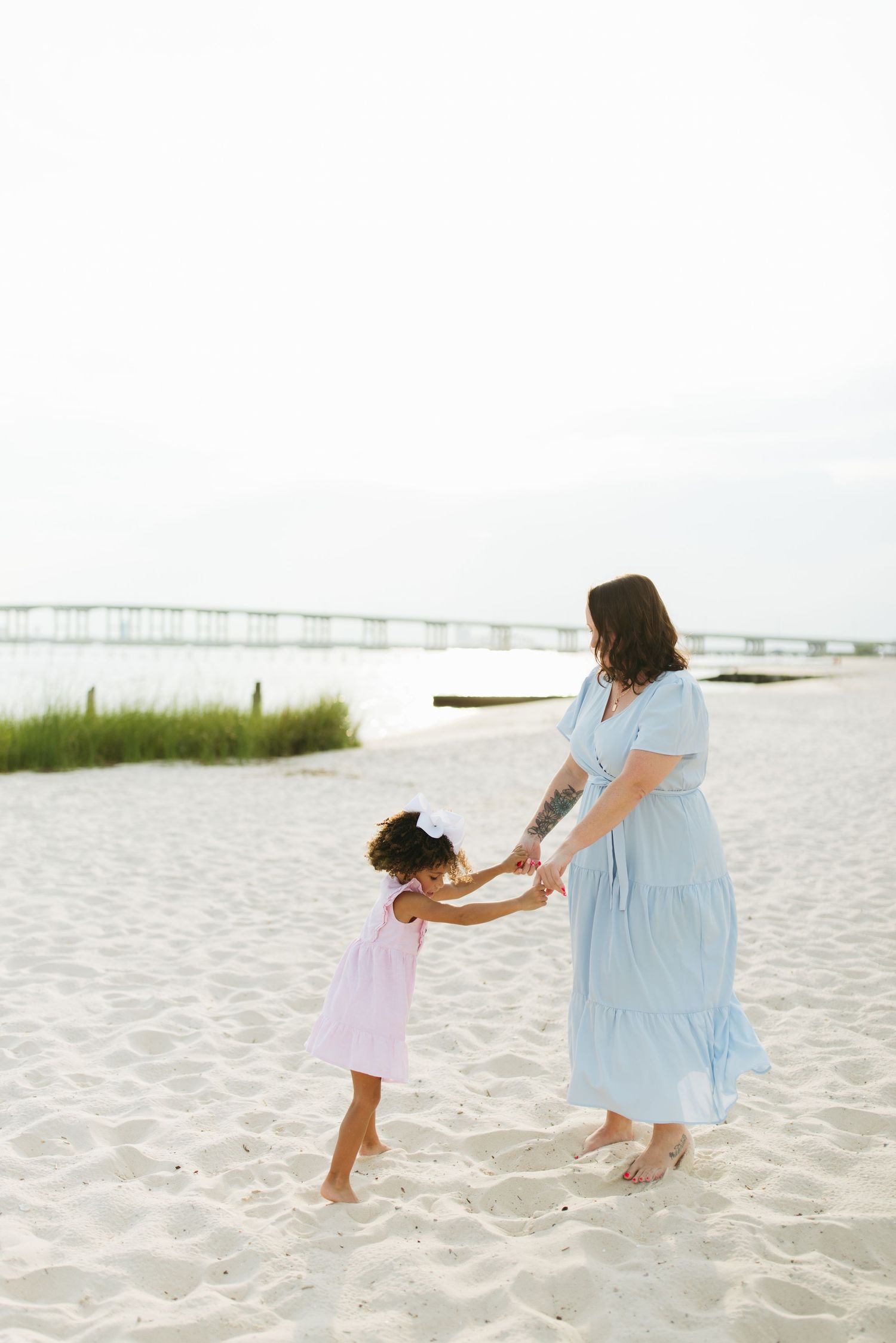 Dancing together on a sandy beach with a pier visible in the background on an overcast day.