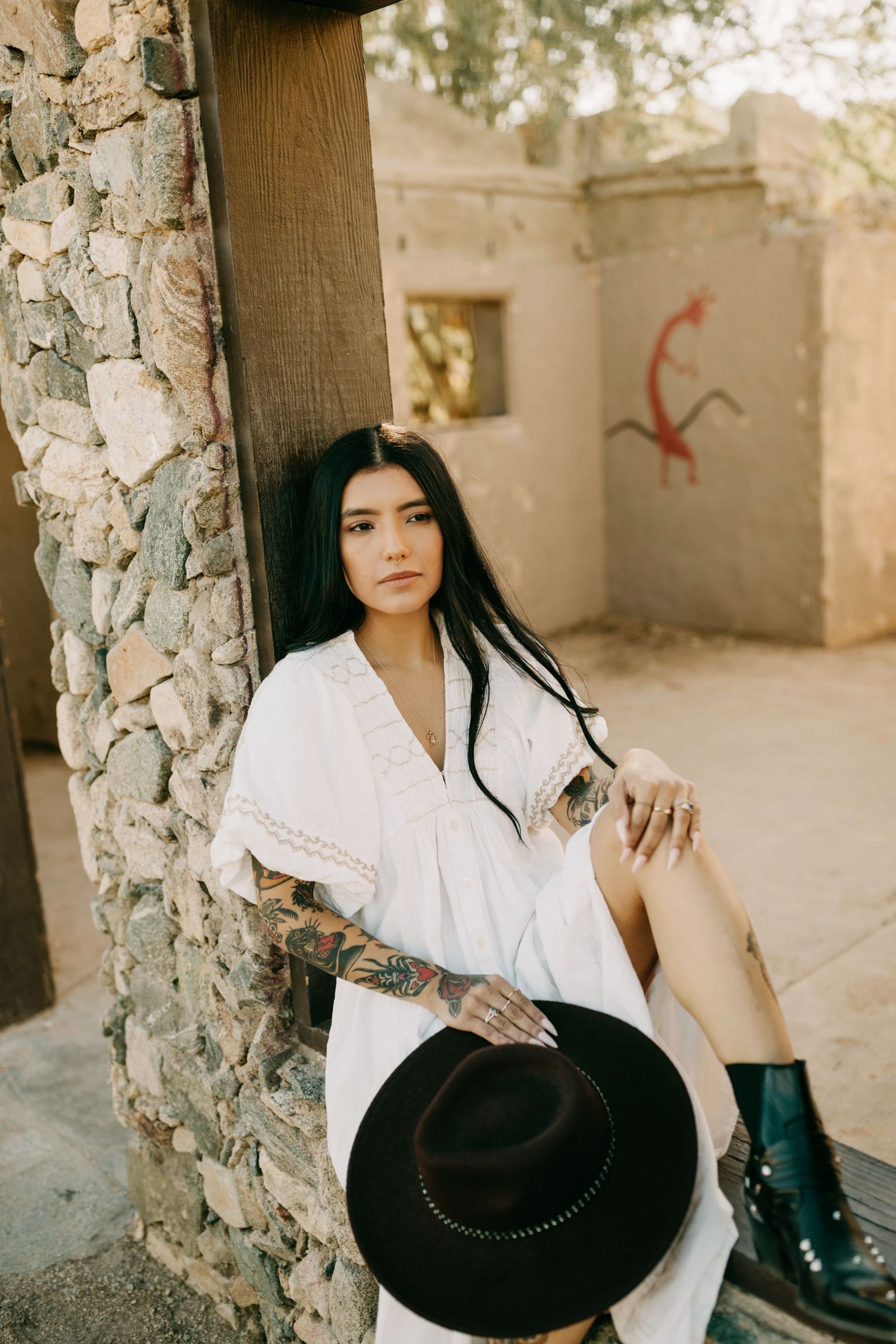 A series of stylized fashion portraits against stone walls featuring a white blouse and black hat in natural lighting.