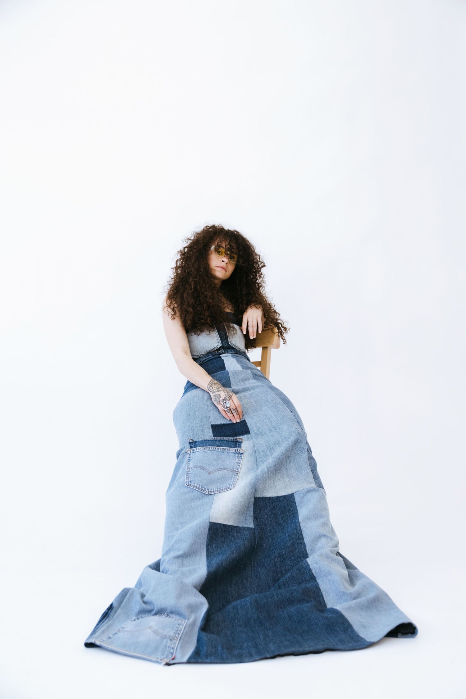 Artistic fashion portrait showing an innovative patchwork denim dress made from recycled jeans against a white backdrop.