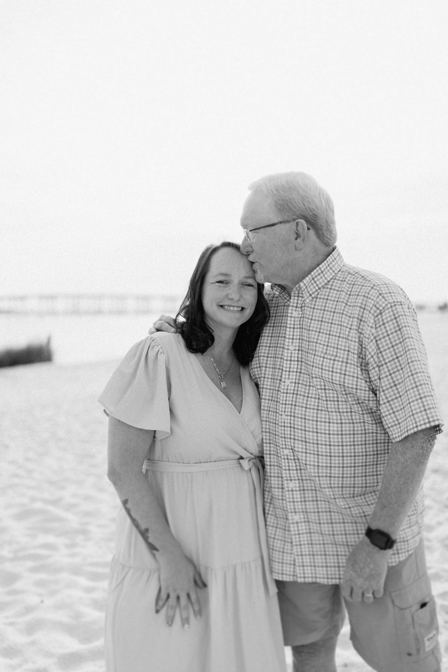 Couple sharing intimate moments during beach photoshoot in casual summer attire.