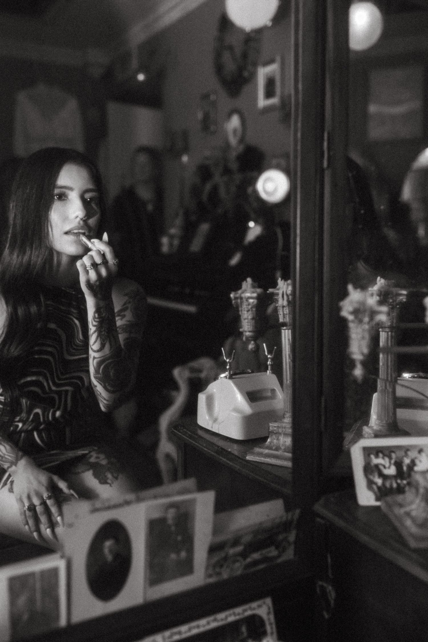 A black and white photo showing someone in reflective thought at a table with vintage decor and decorative bottles.