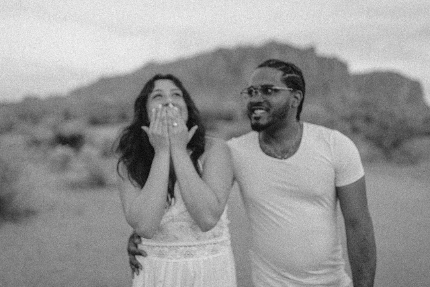 Black and white portrait of a couple laughing and expressing joy together in a desert landscape setting.