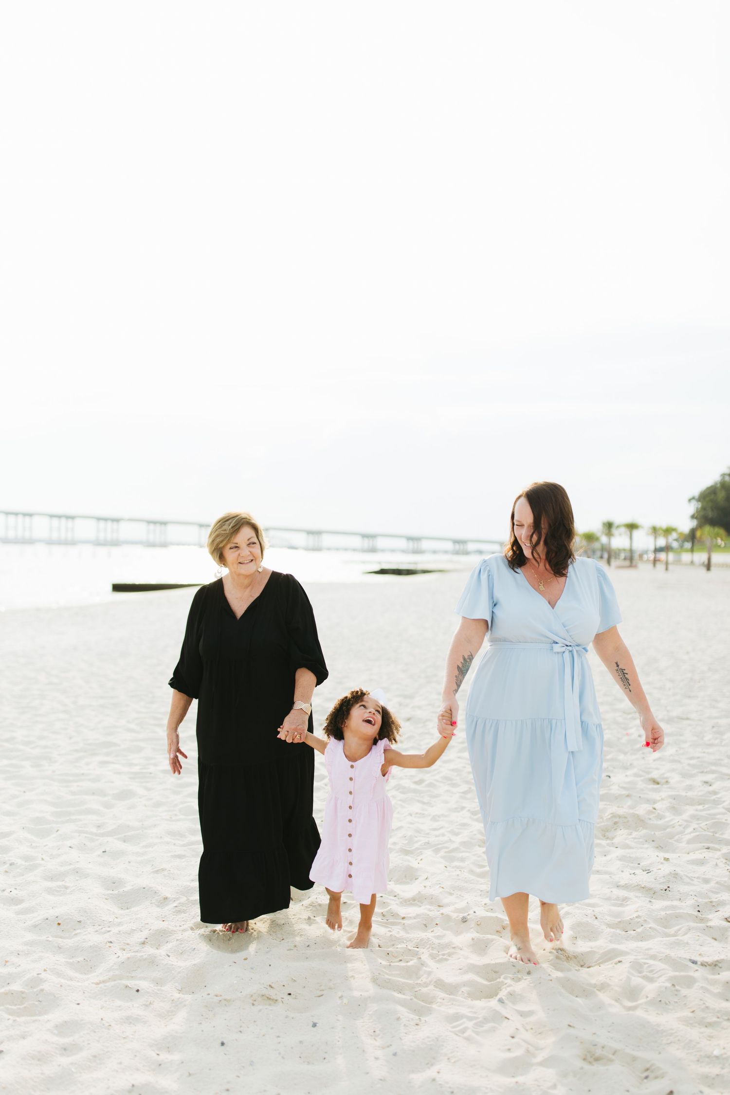 Three people walking together on a white sandy beach with ocean pier in background.