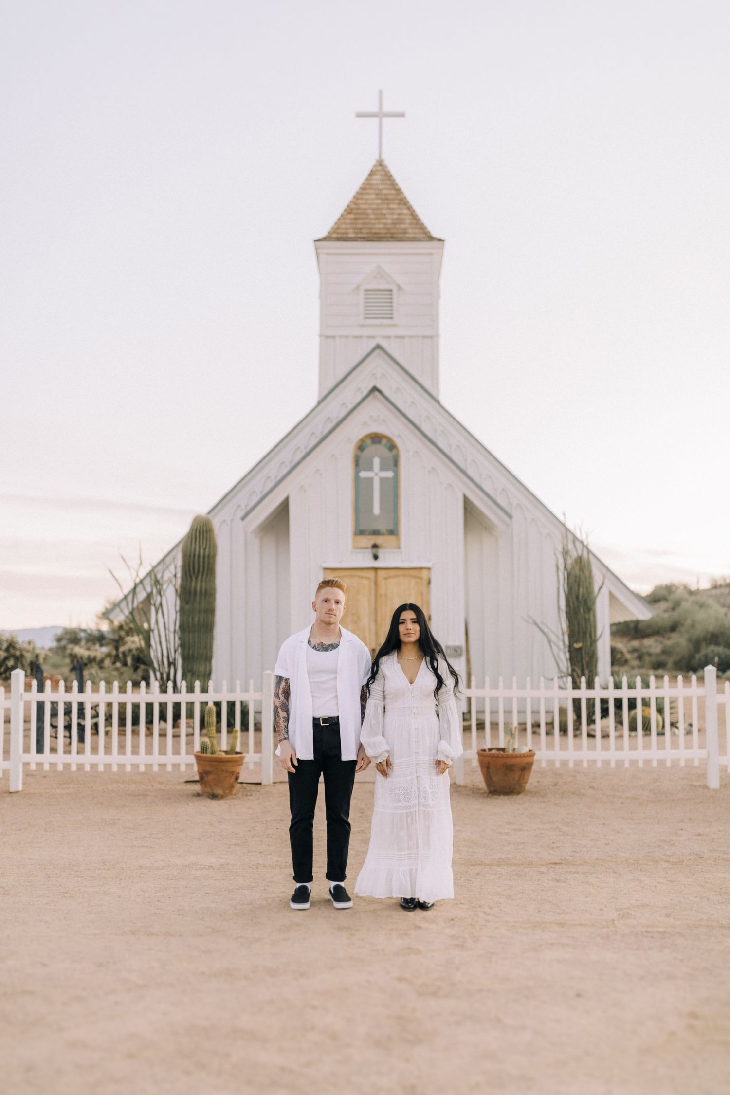 Five sequential photos of a couple walking by a small white chapel with a cross and white picket fence in a desert setting.