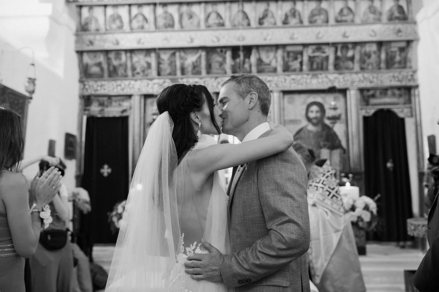 A romantic black and white moment between newlyweds sharing a kiss at the altar with an ornate reredos in the background.