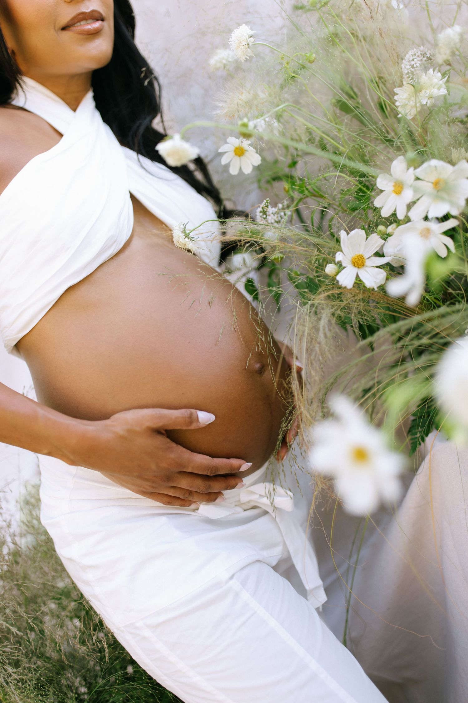 An artistic maternity photo with white daisies and flowing fabric against a light background.
