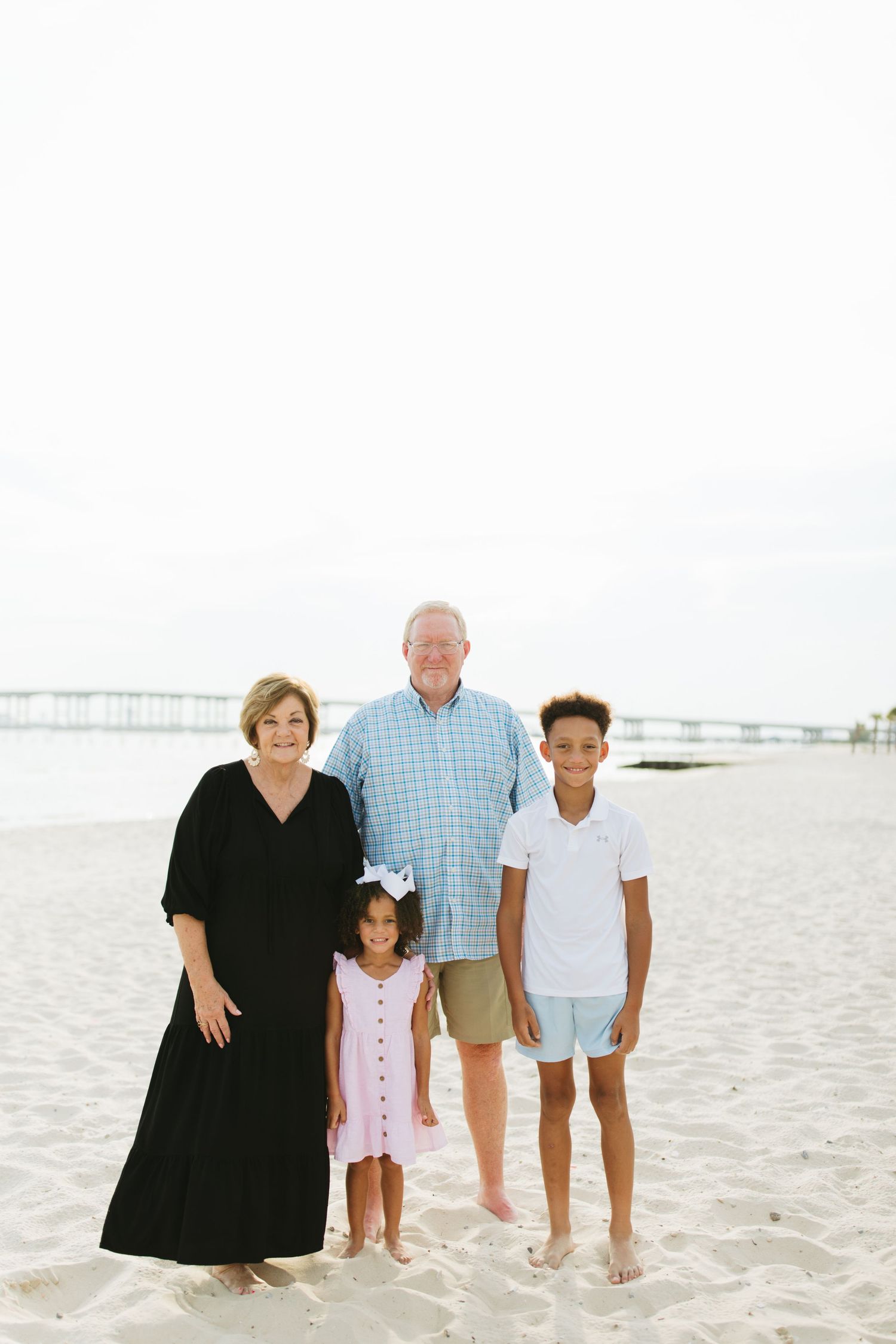 Family enjoying a casual beach photo session together on white sand with pier in background.
