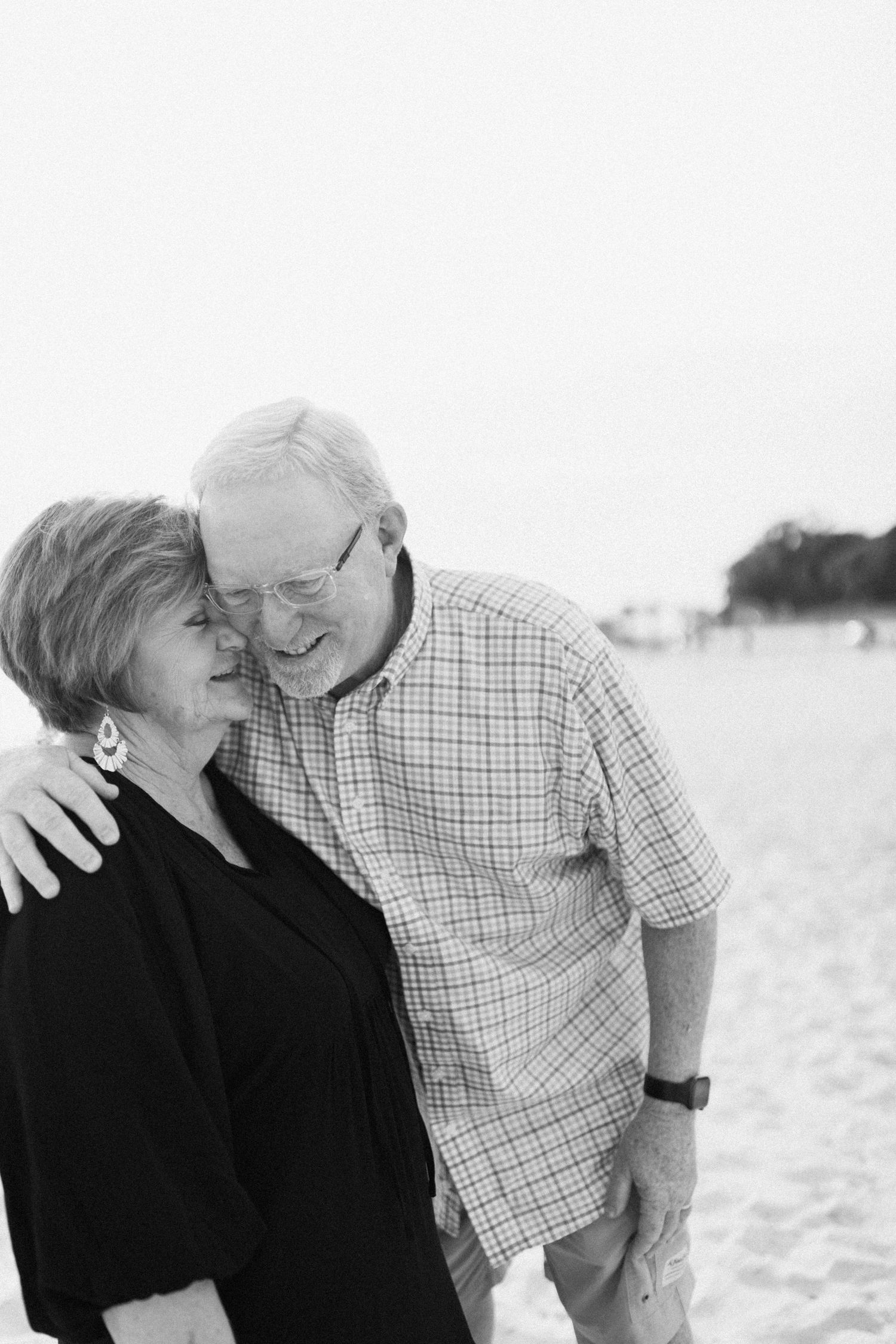 Elderly couple embraces and laughs together on bright sandy beach.