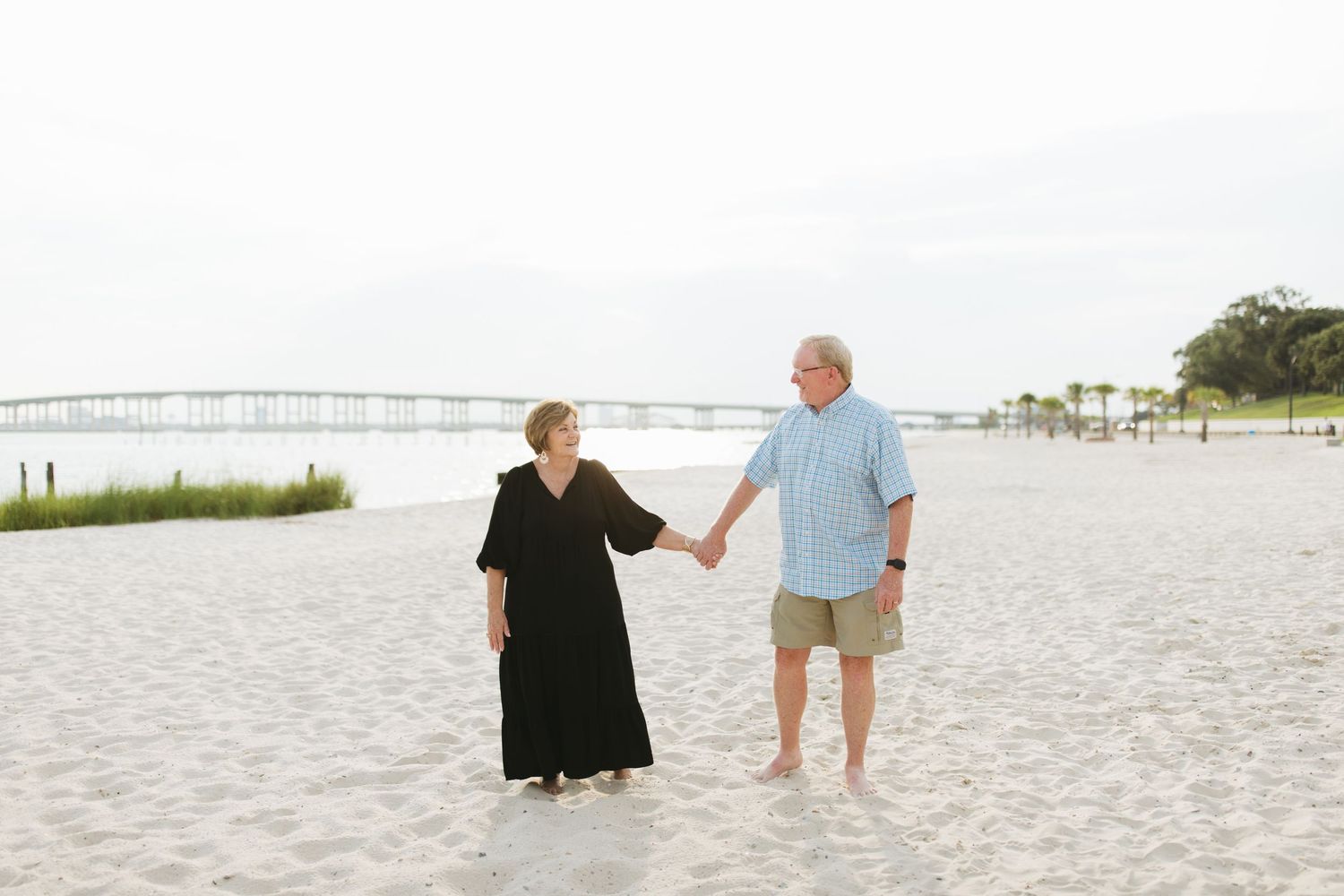 Picturesque beach scene showing small figures walking along white sand with a pier in the distance.