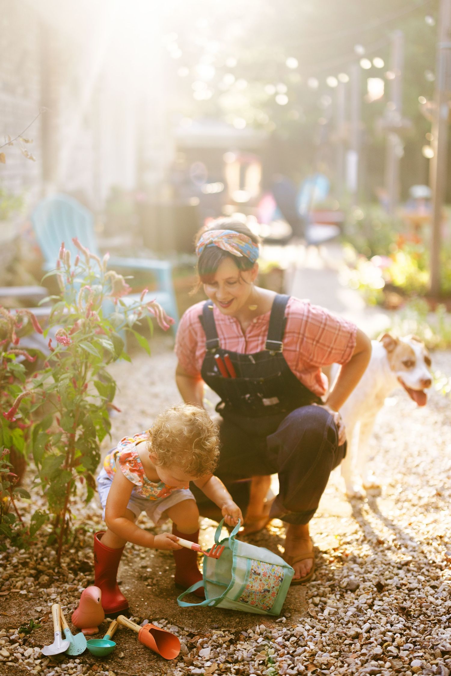 Two small children in overalls gardening together in dappled sunlight and fallen leaves.