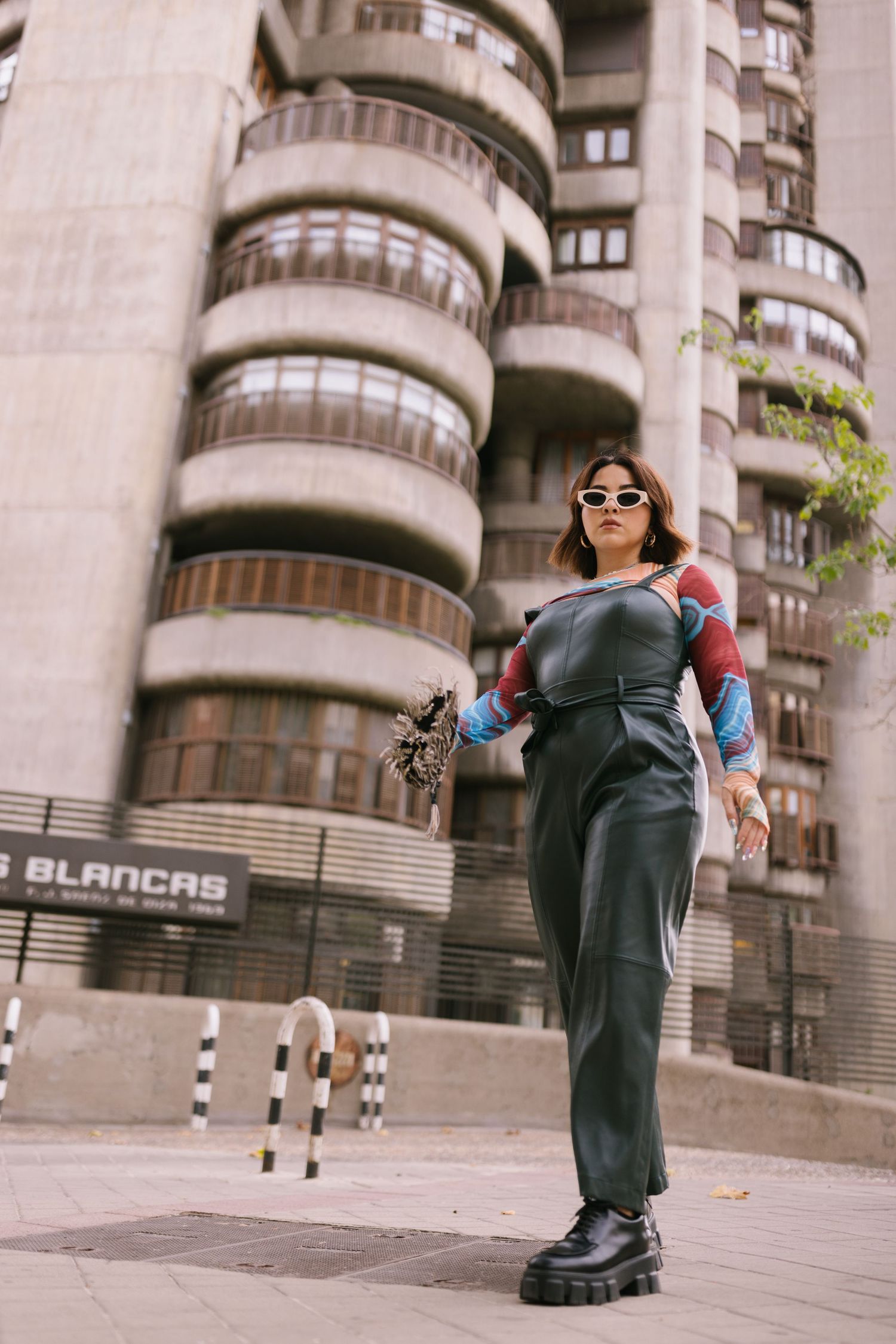 Person wearing chunky black platform boots and baggy jeans poses in front of modern apartment building with curved balconies.
