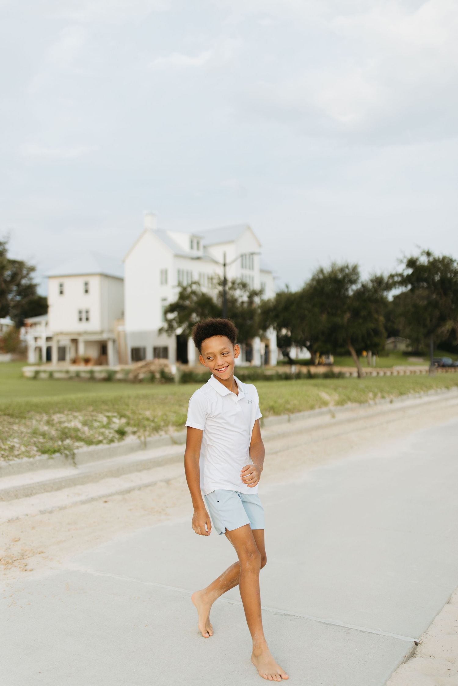 Child playing and jumping on a sandy path with white coastal houses in the background.