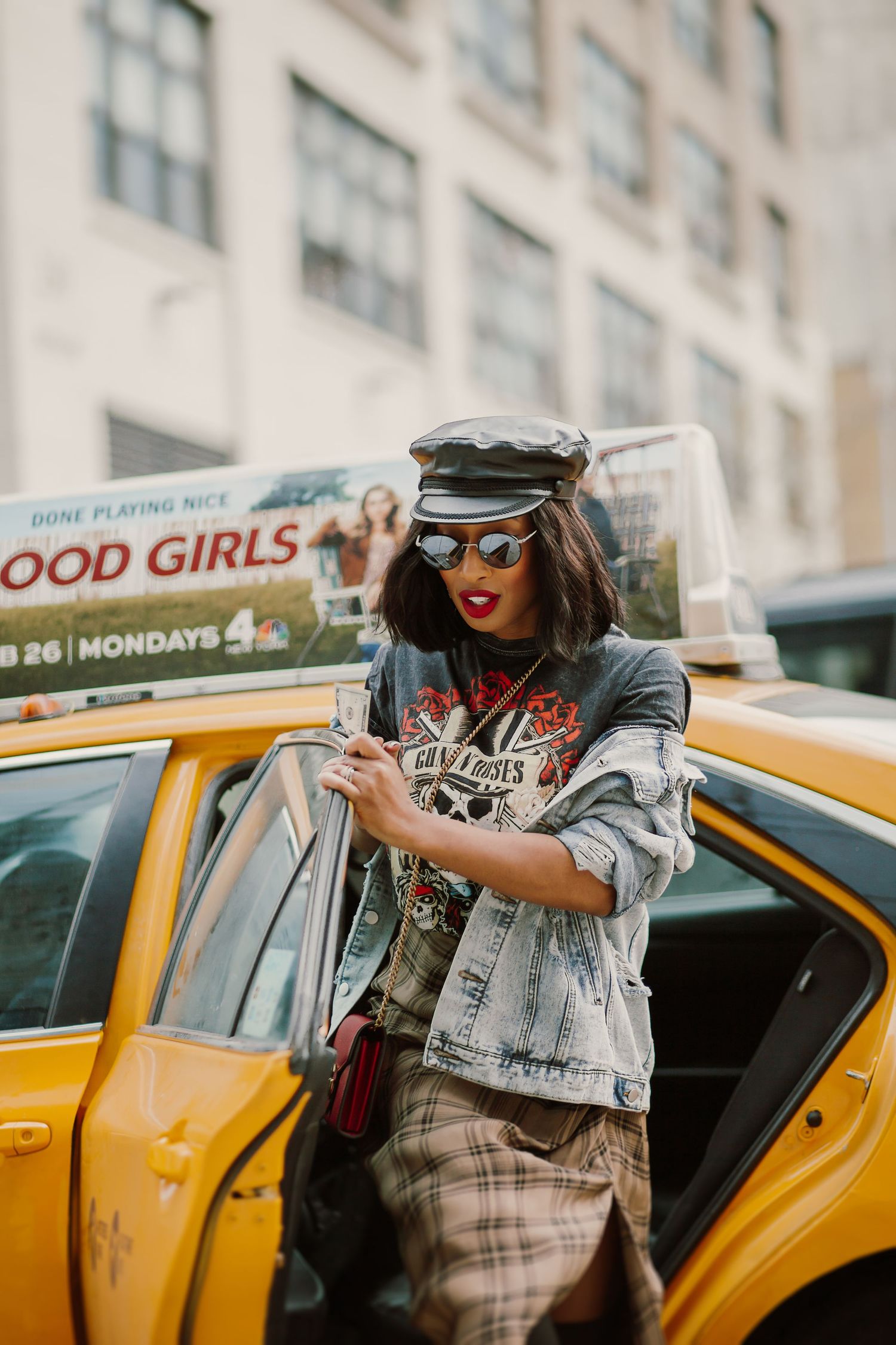 Stylish traveler with red lipstick and sunglasses stepping out of a yellow NYC taxi cab in an urban setting.