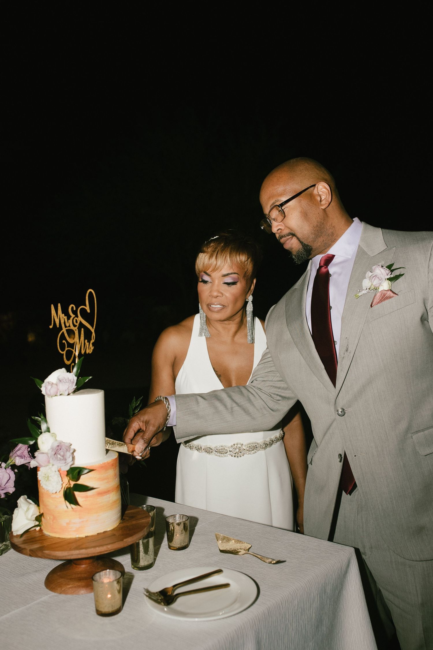 A couple cuts their elegant two-tier wedding cake with peach ombre design and floral decorations at their reception.