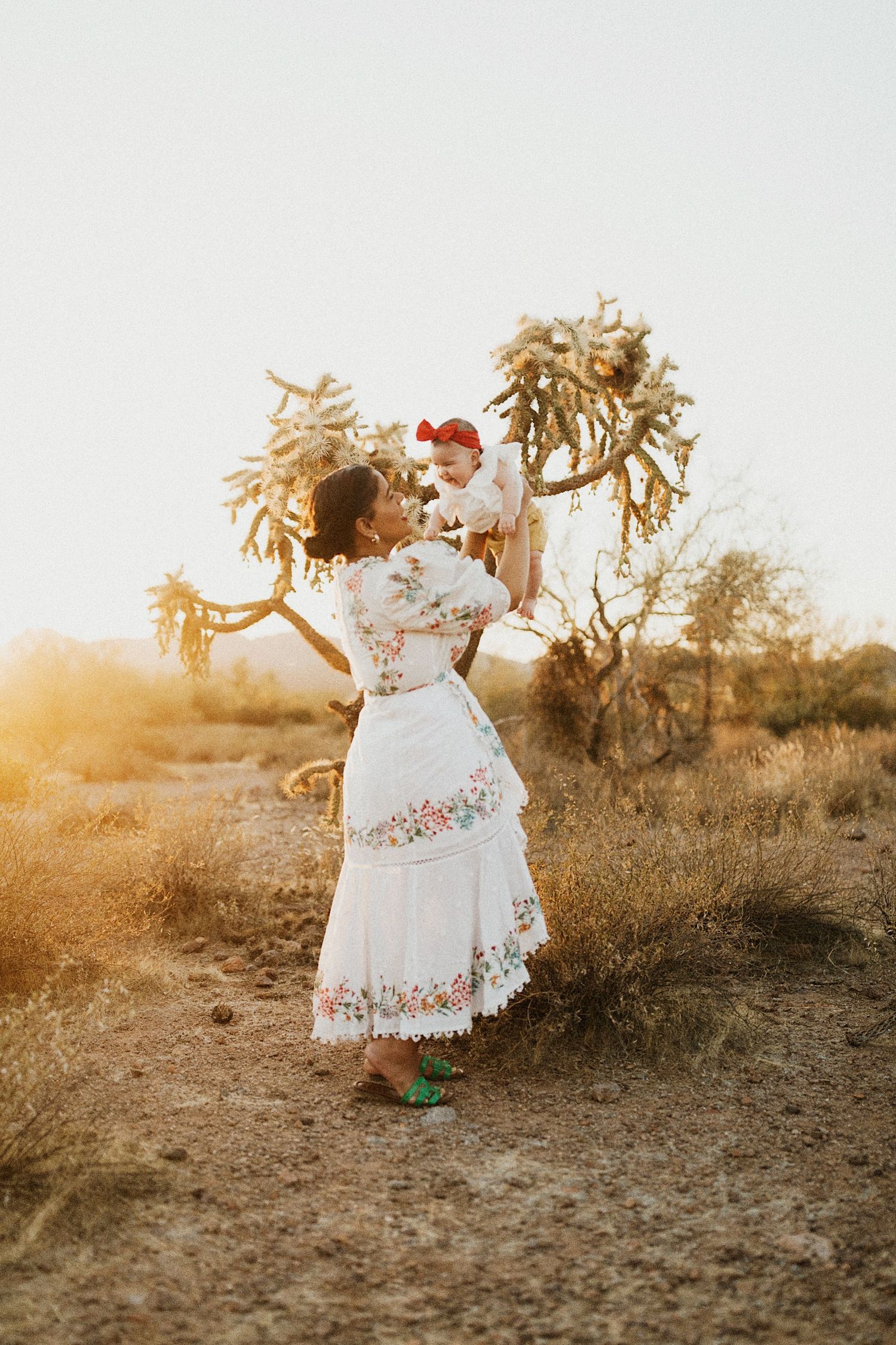 A person in a white embroidered Mexican dress dances with dried wheat stalks in a golden desert sunset.