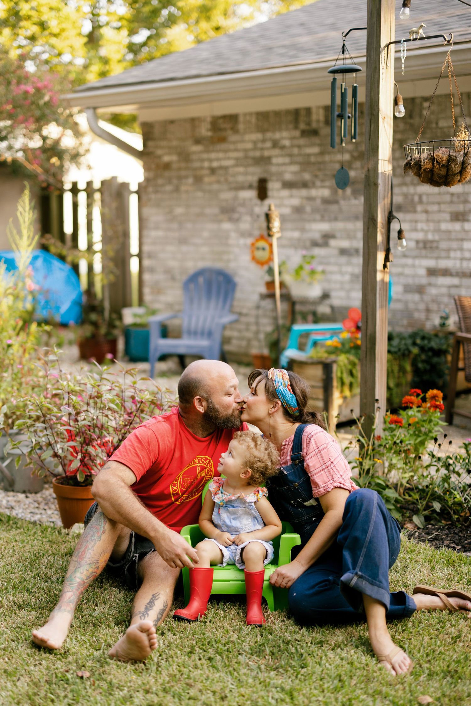 Family relaxation time on a lawn near a brick house with blue patio furniture and hanging plants.