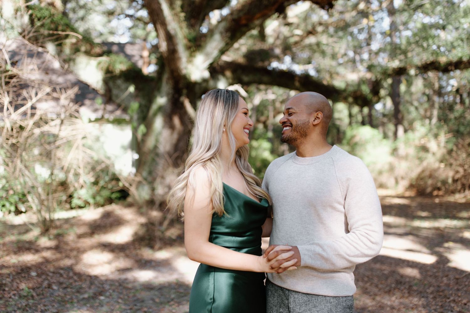 A couple in love share a romantic moment in a sunny wooded park, with her wearing an emerald green dress.