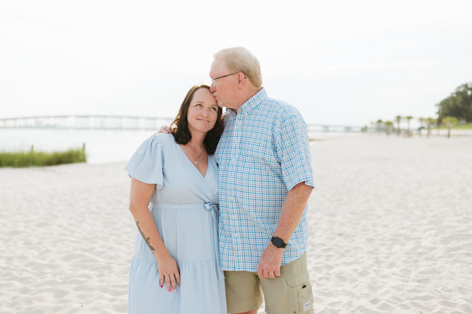Three people share an embrace while standing together on a pristine beach with coastal vegetation.