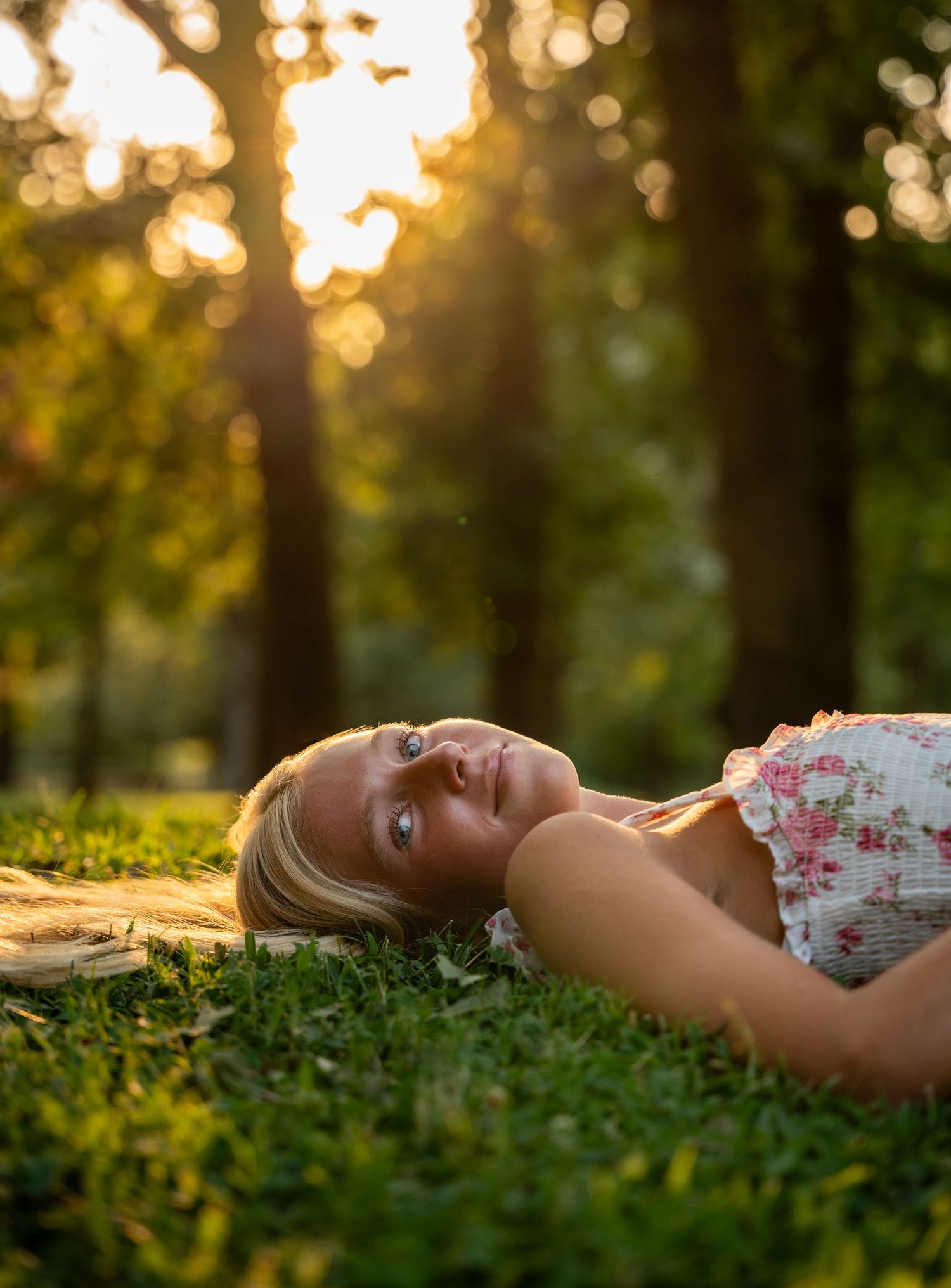 Person lying peacefully in green grass during golden sunset with dreamy bokeh light effects in background.