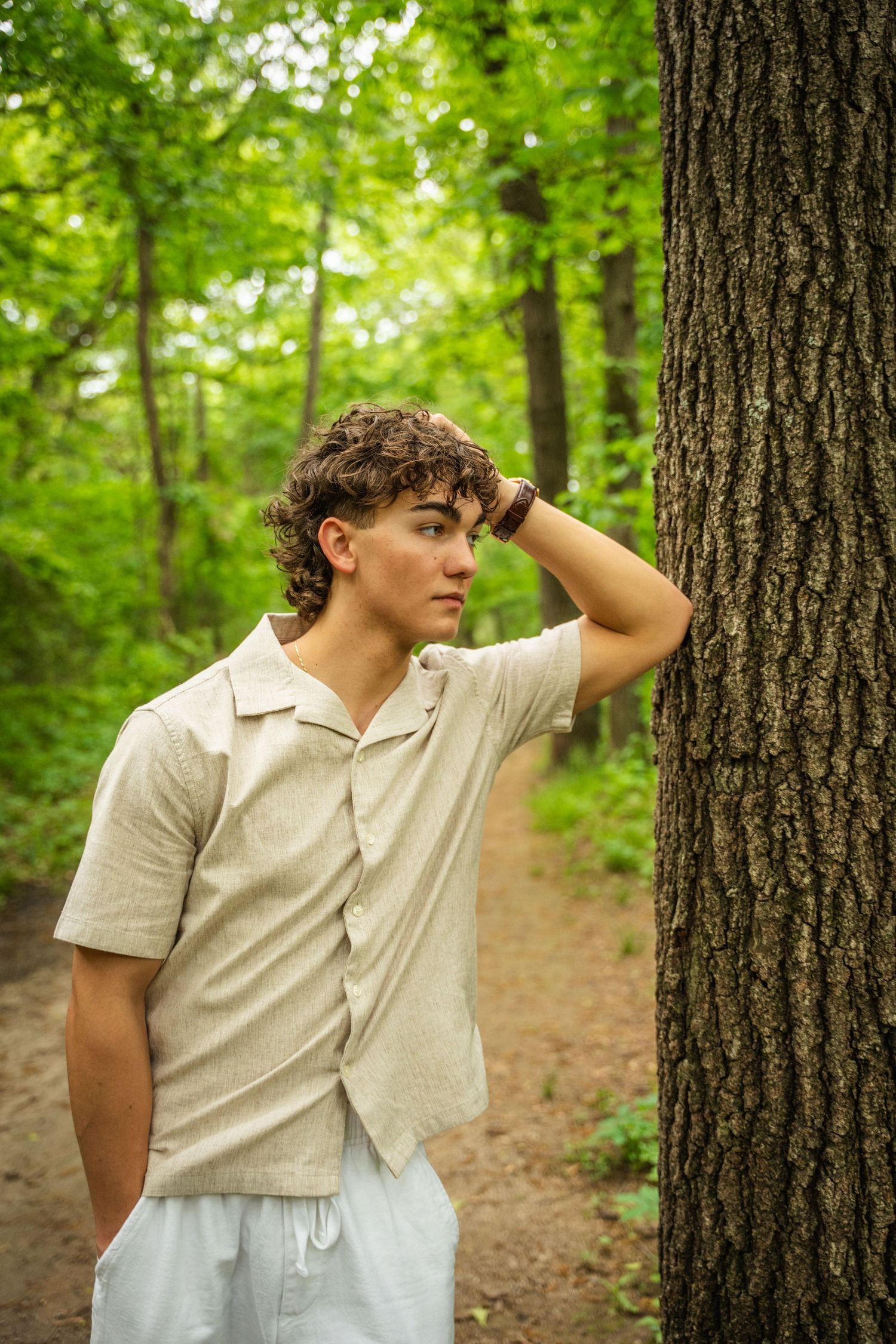 Portrait series of person in beige shirt posed against tree trunk in lush forest setting.