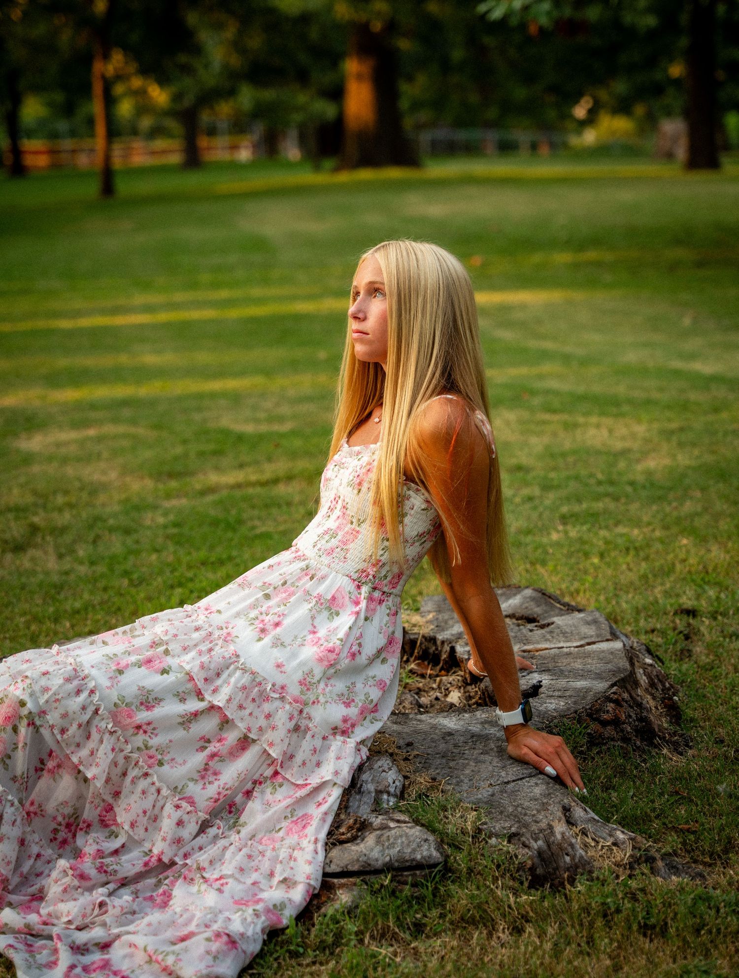 A person in a floral dress reclines on a large rock formation in a grassy outdoor setting.