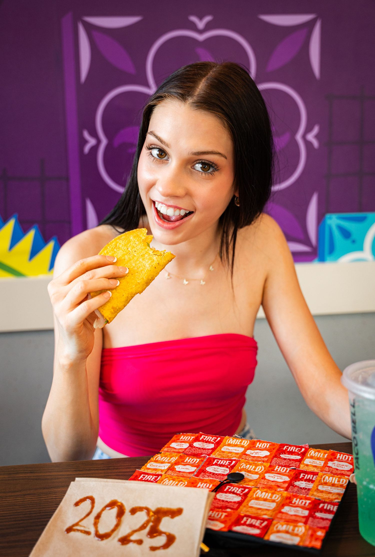 Colorful photo with someone eating a taco against purple decorative background.