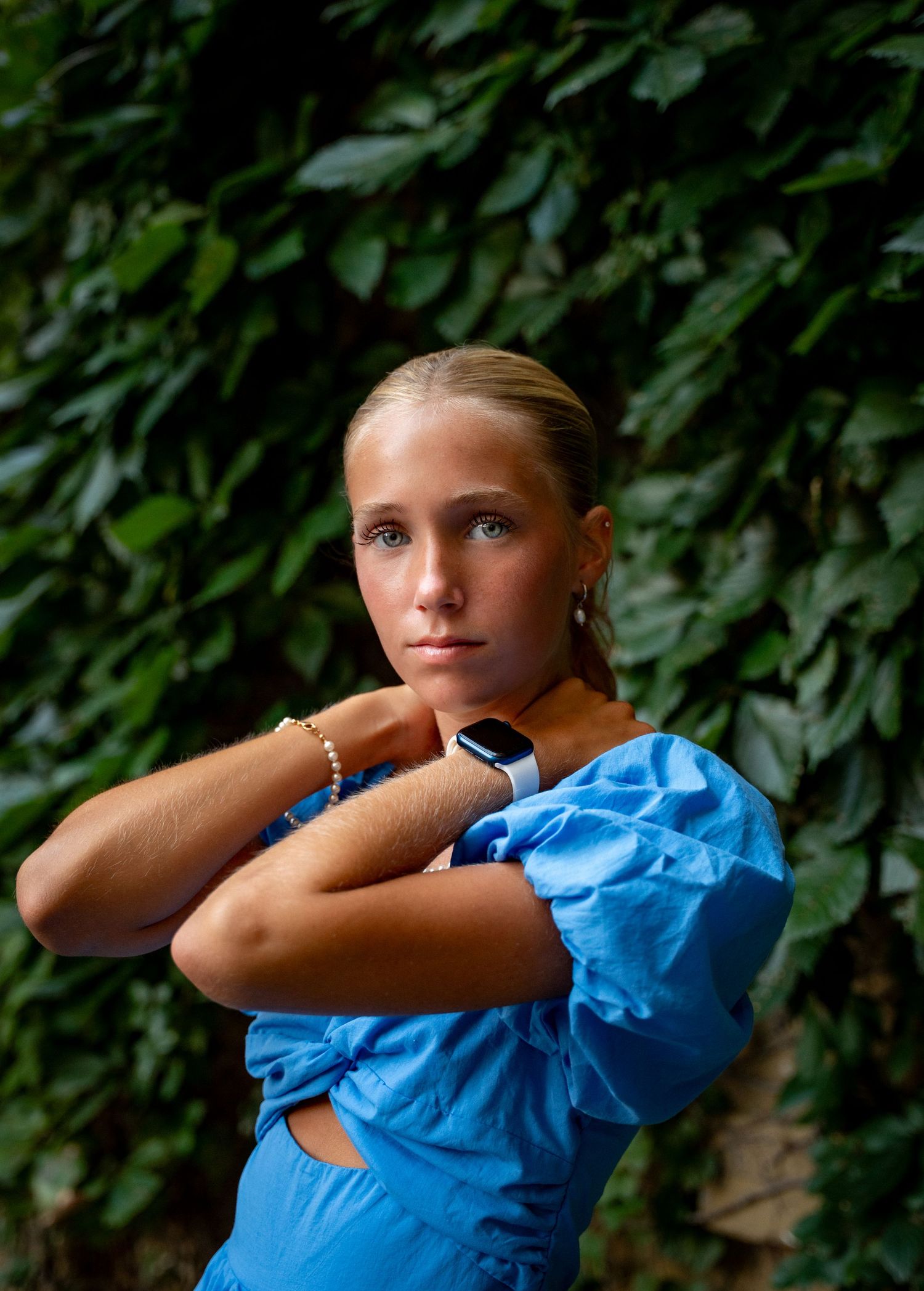 Person in bright turquoise puff-sleeve dress poses against lush green foliage background.