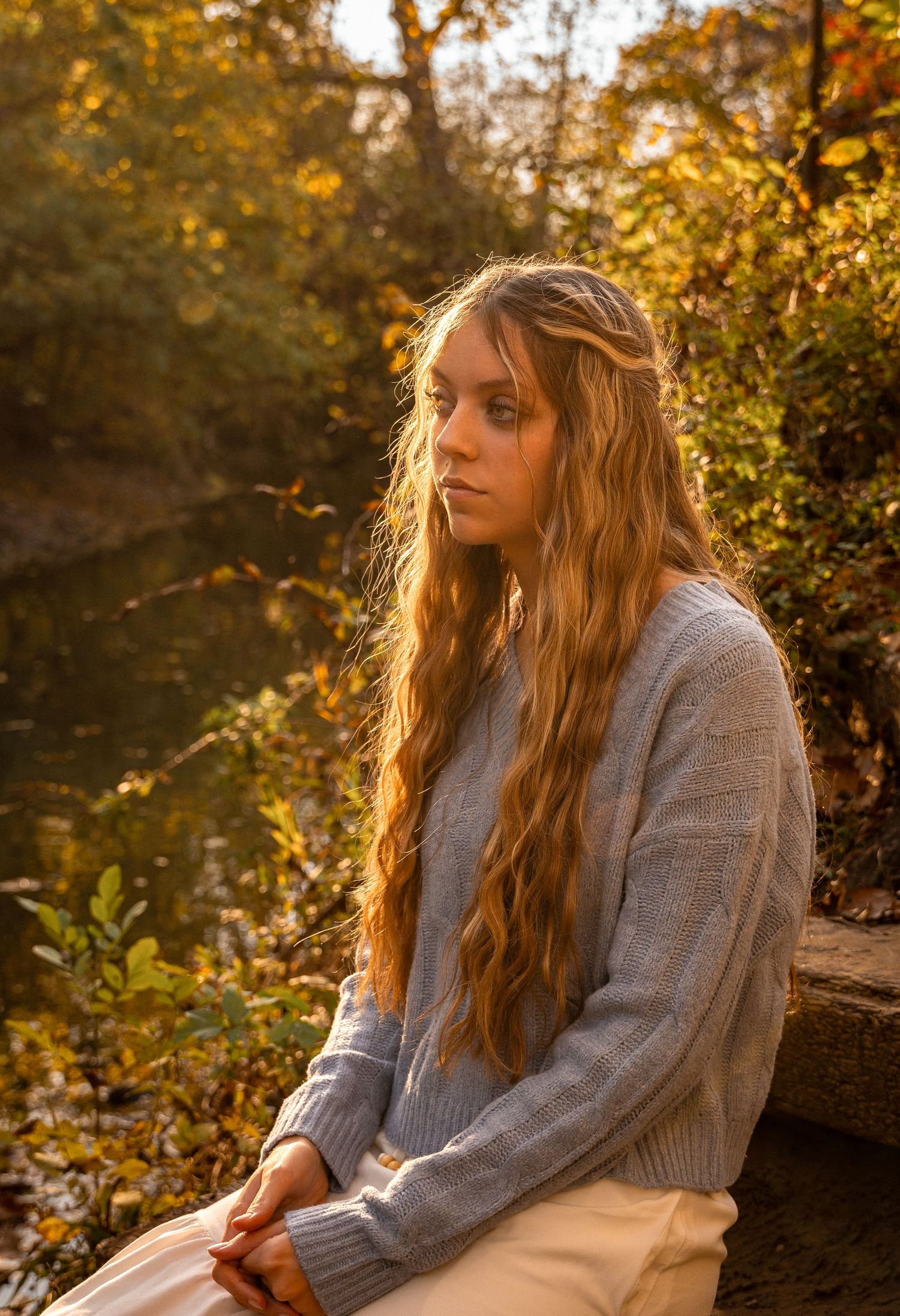 Person in grey sweater posed outdoors during golden hour autumn lighting.