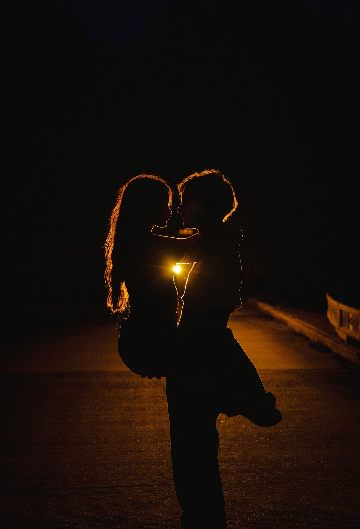 A silhouetted couple embracing at night illuminated by a warm glowing light.