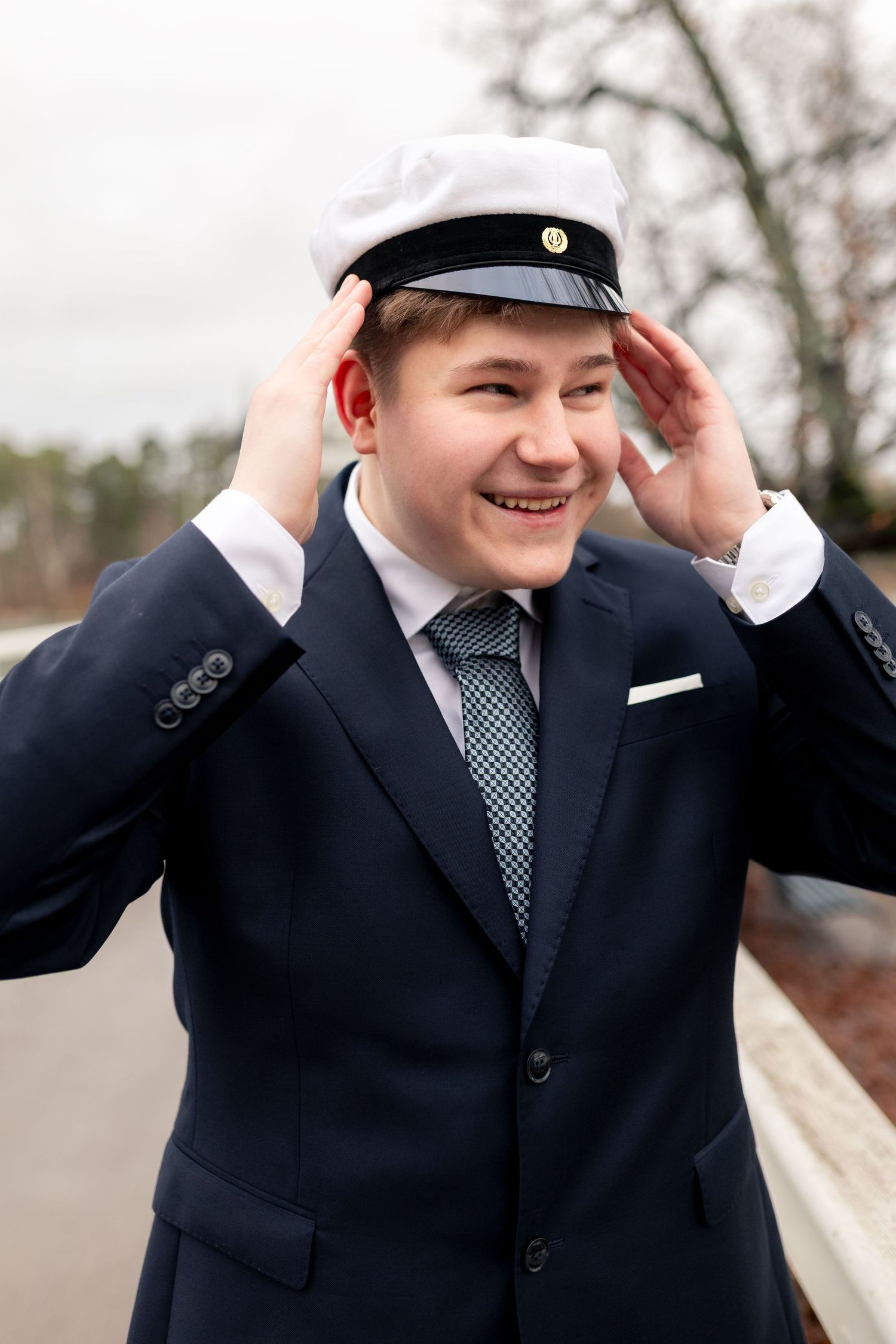 Poika puvussa oikoo lakkiaan- ylioppilaskuvaus