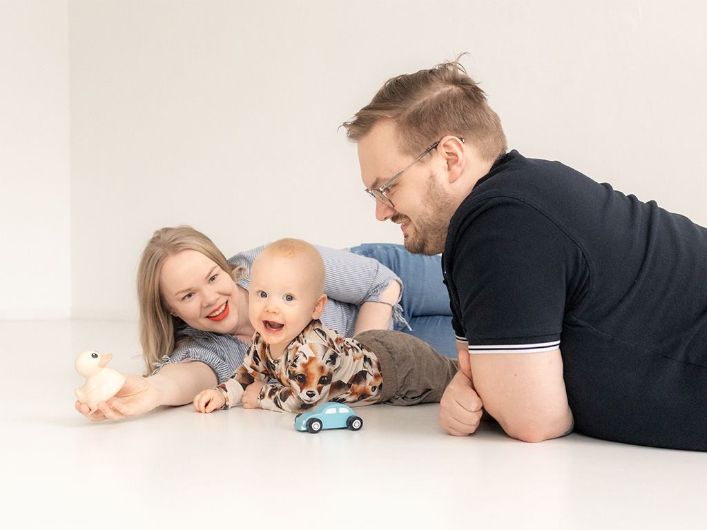 Vanhemmat makoilee vauvan kanssa lattialla perhekuvauksessa Helsingissä