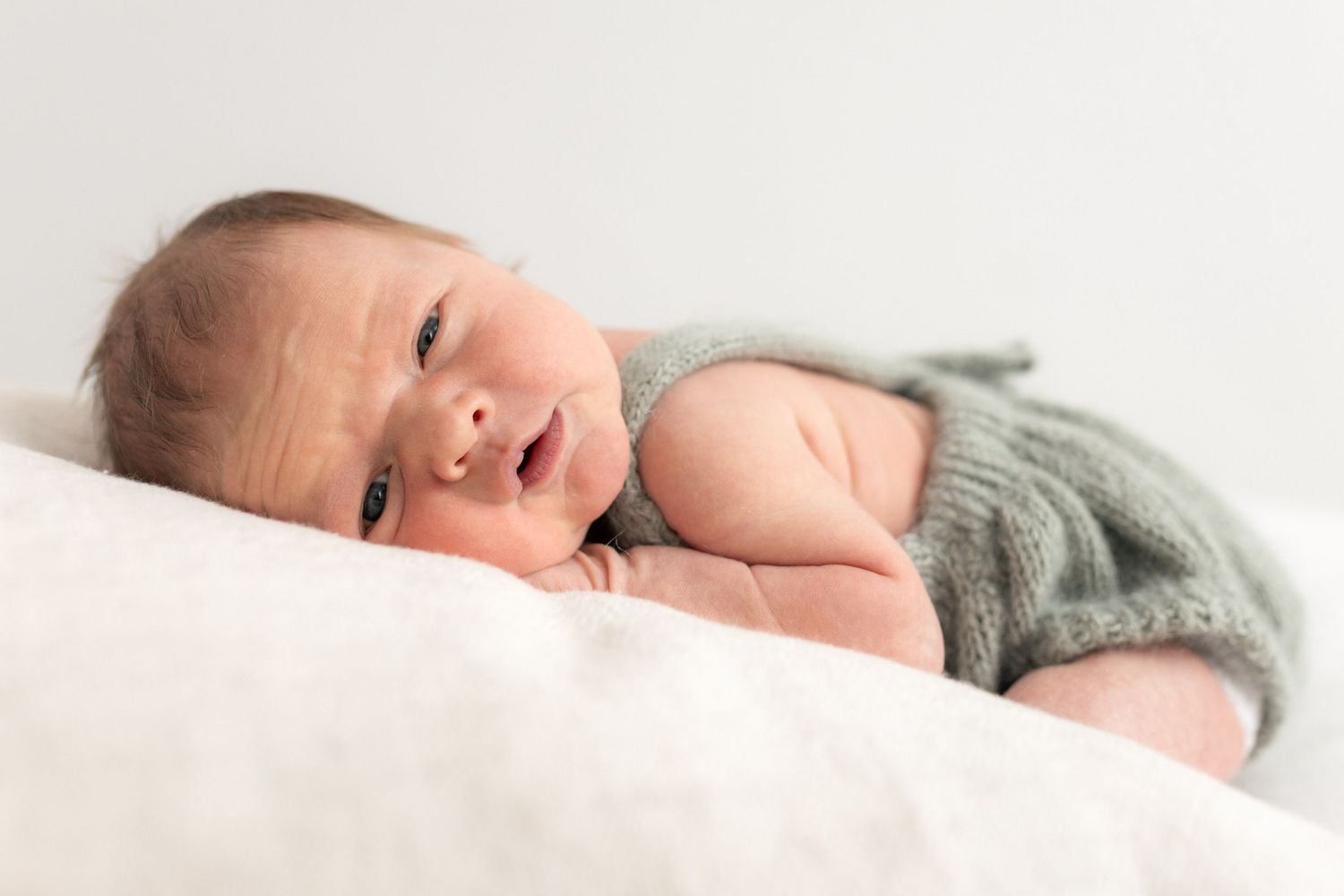 Vastasyntynyt vauva vihreässä neulotussa asussa newborn kuvaus