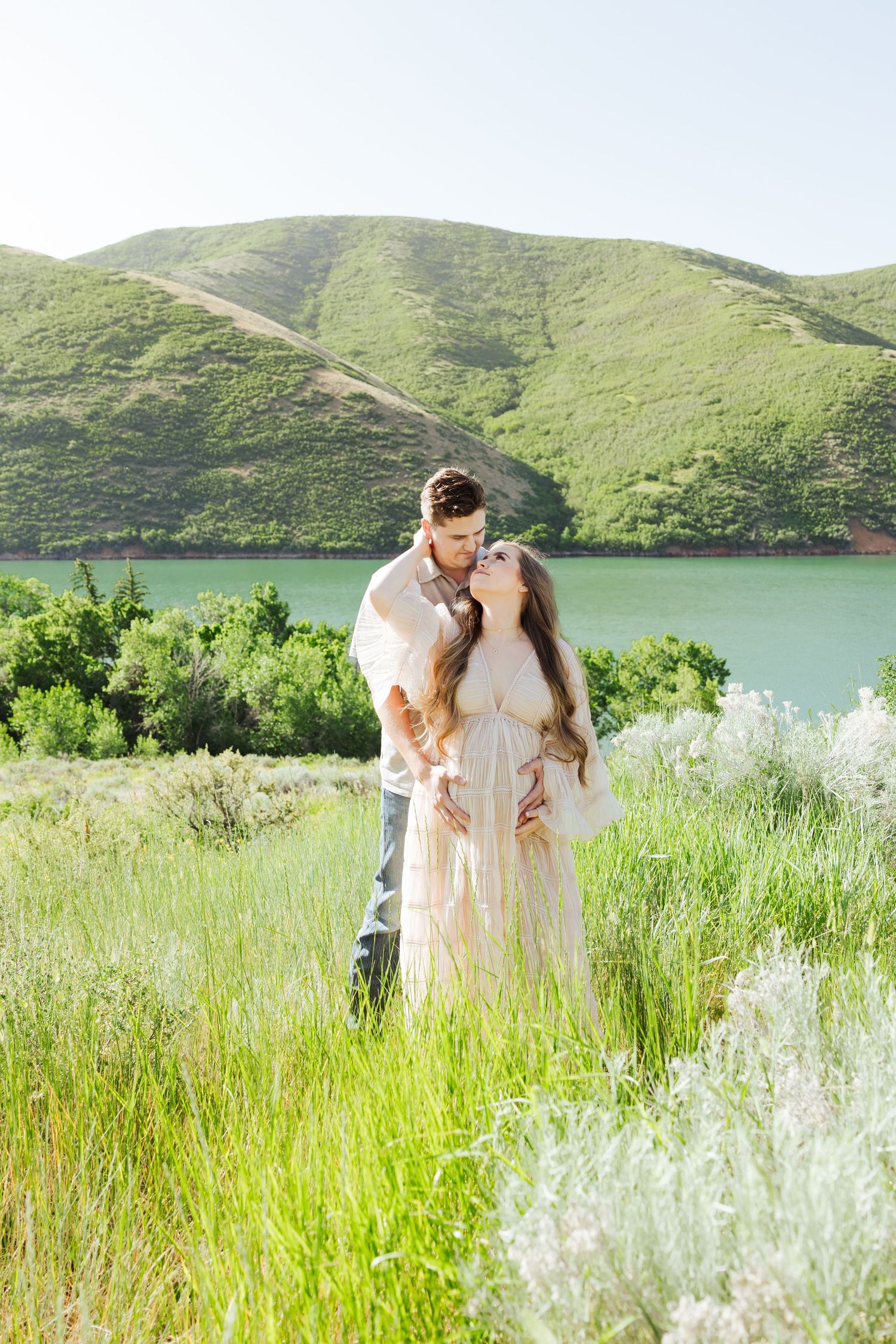 Pregnant woman with husband in field at Little Dell Reservoir photography by Av Potter Photo a Utah wedding and lifestyle photographer