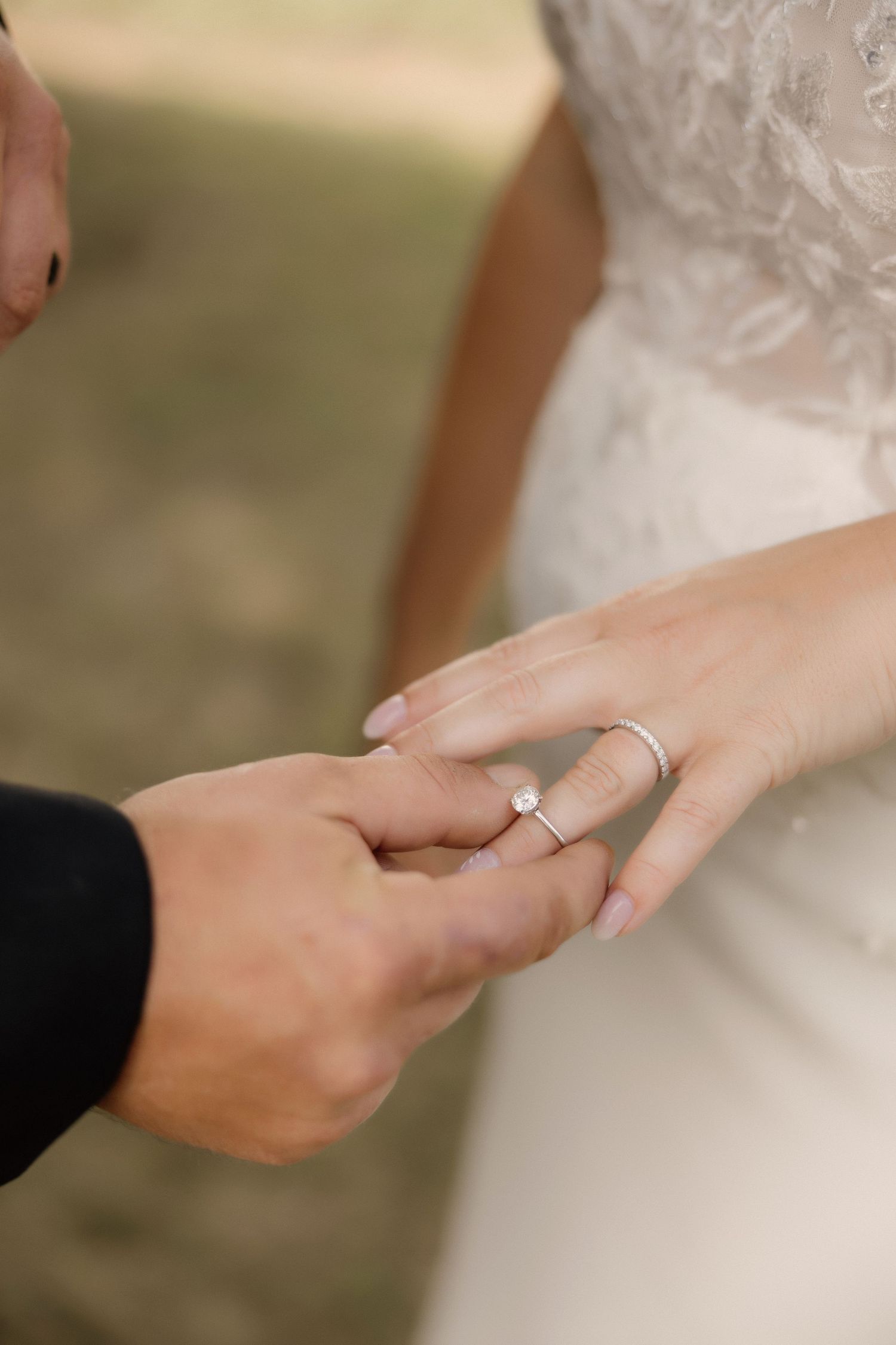 Close-up of wedding ring exchange with bride in lace dress.