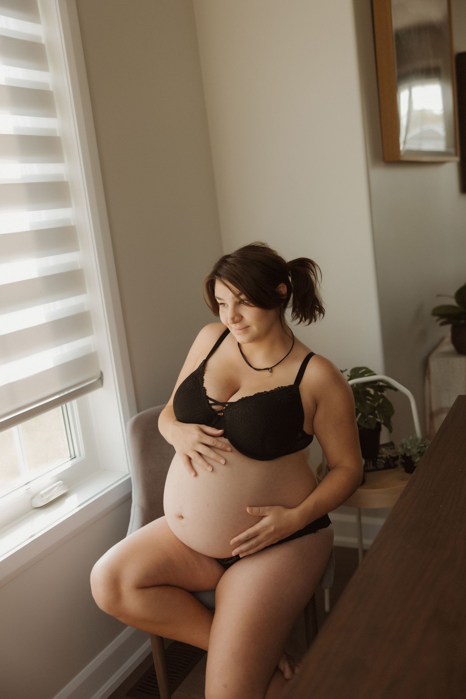 A maternity portrait by a window showing an expectant mother in black loungewear.