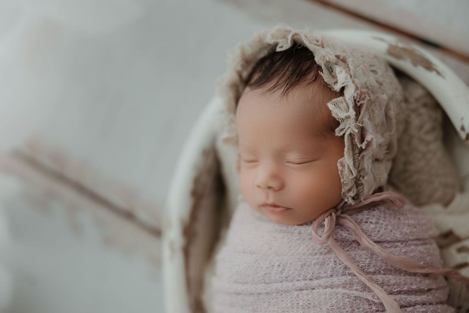 Peaceful sleeping newborn wearing delicate lace bonnet and pink wrap.