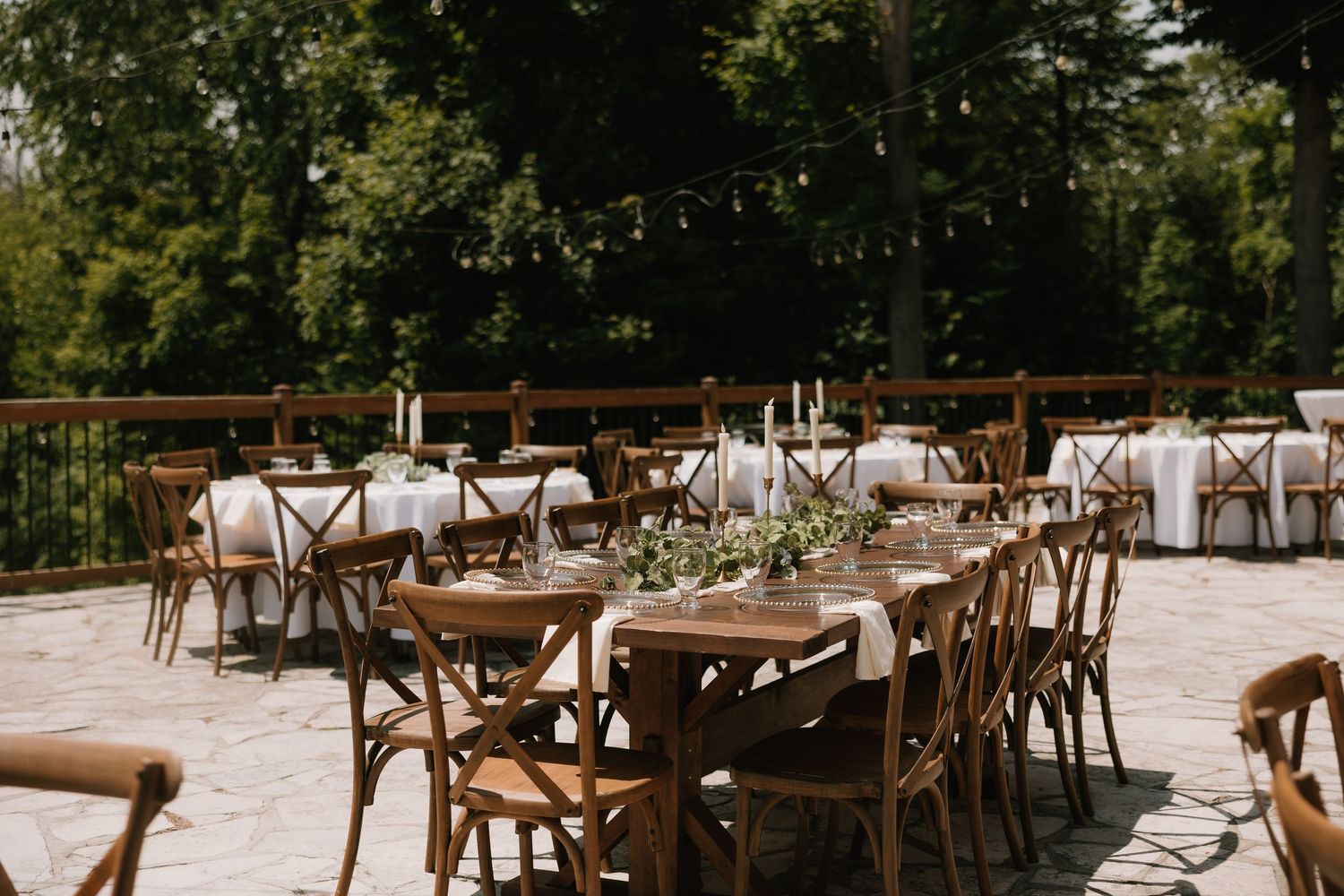 Elegant outdoor wedding reception setup with wooden cross-back chairs and white tablecloths.