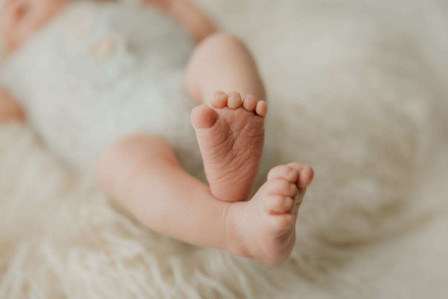 Close-up of tiny newborn baby feet against soft white bedding.