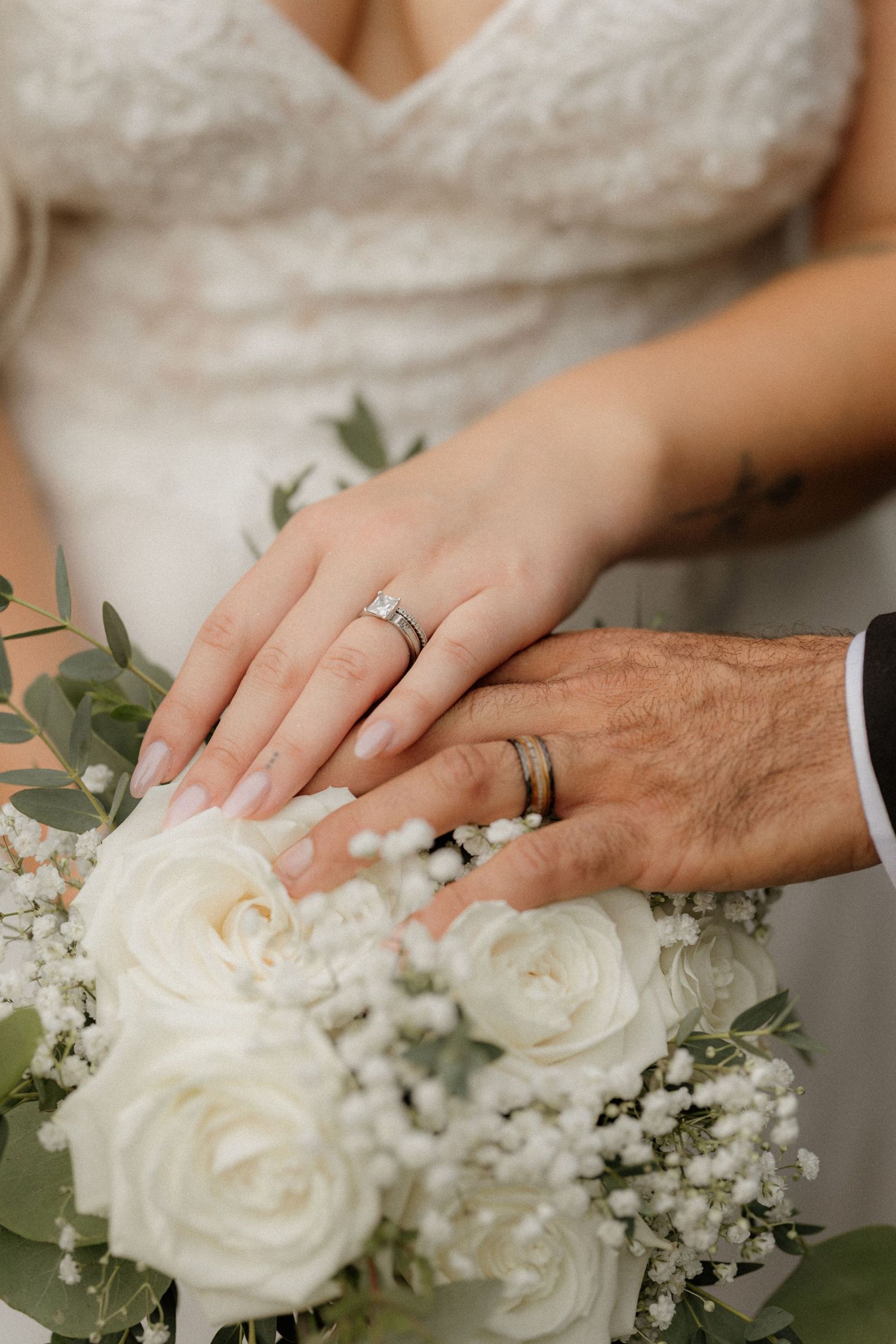 Newlyweds display their wedding rings against a white rose and baby's breath bouquet.