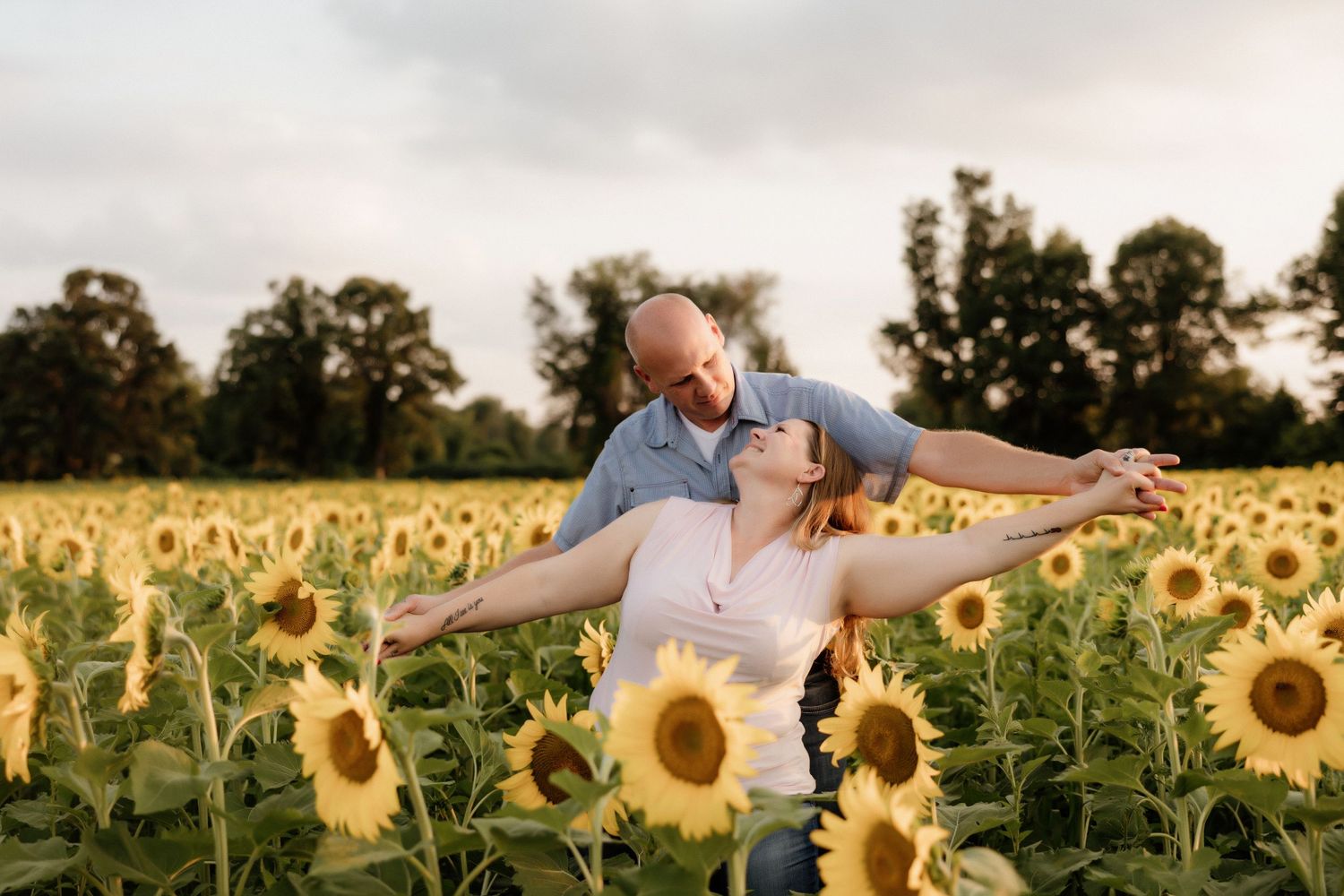 Playful couple embracing in a vibrant sunflower field at sunset.