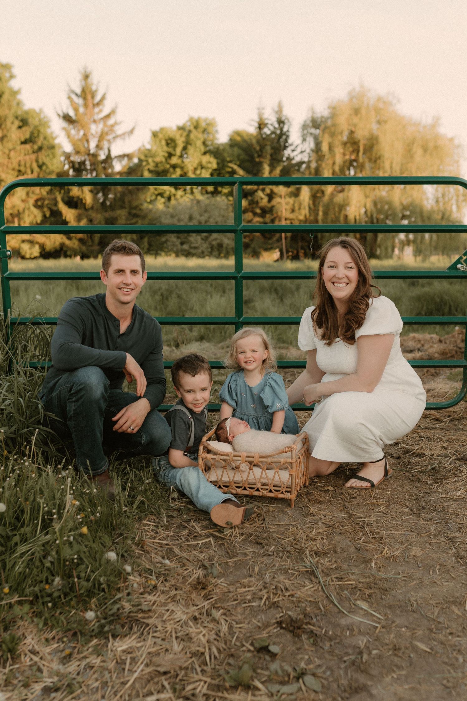 Family sits together by rustic green gate during outdoor photo session.