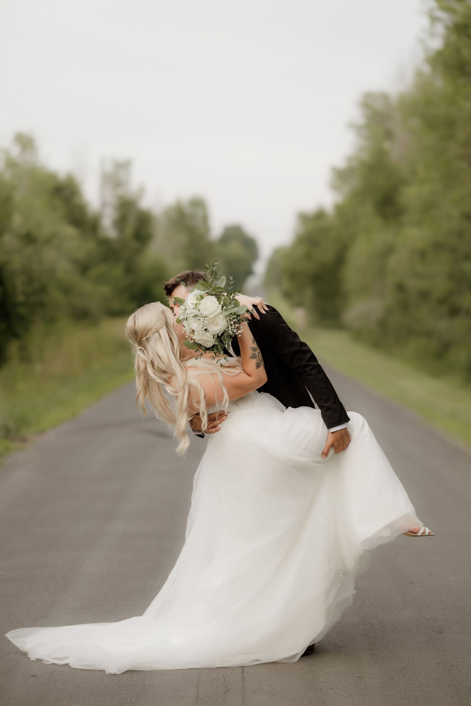 Romantic wedding couple kissing and dipping on a country road with white dress flowing.