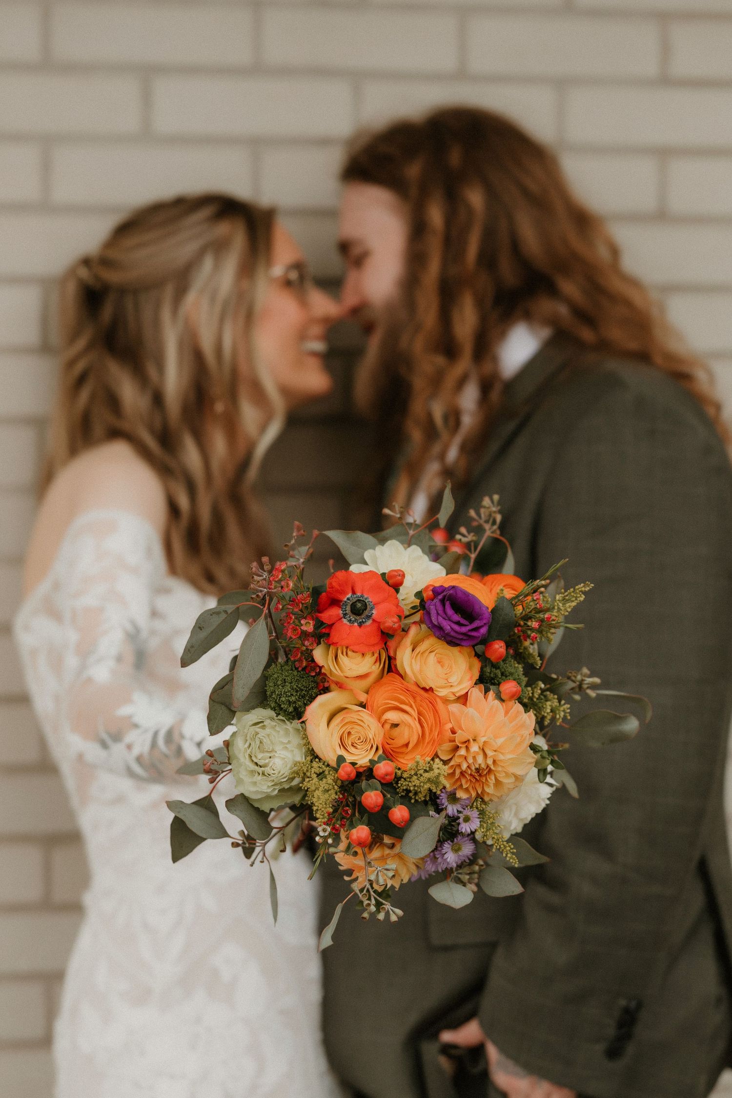 A romantic wedding portrait with vibrant orange and purple floral bouquet against white brick.