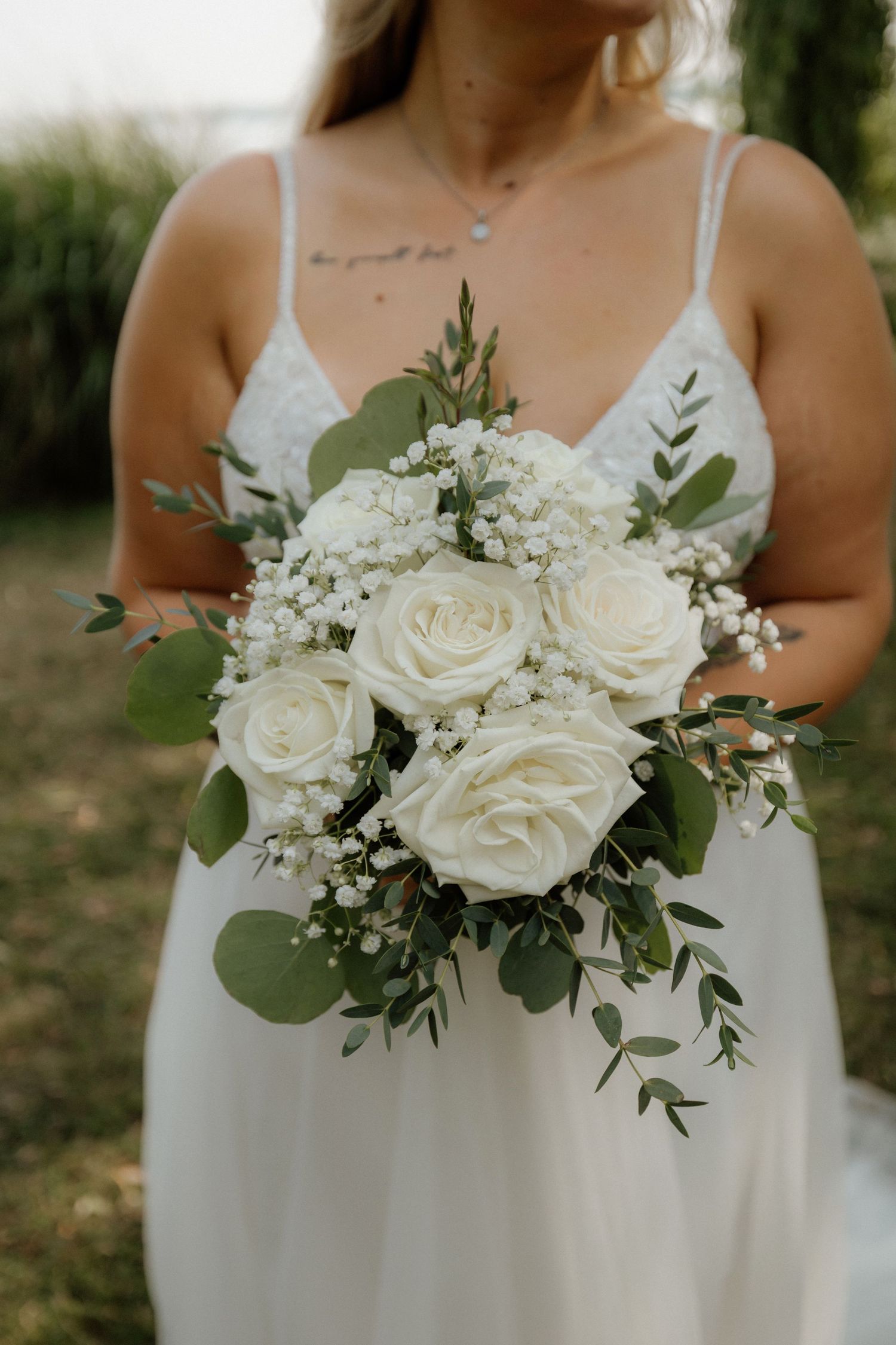 White rose wedding bouquet with eucalyptus leaves and baby's breath against white dress.