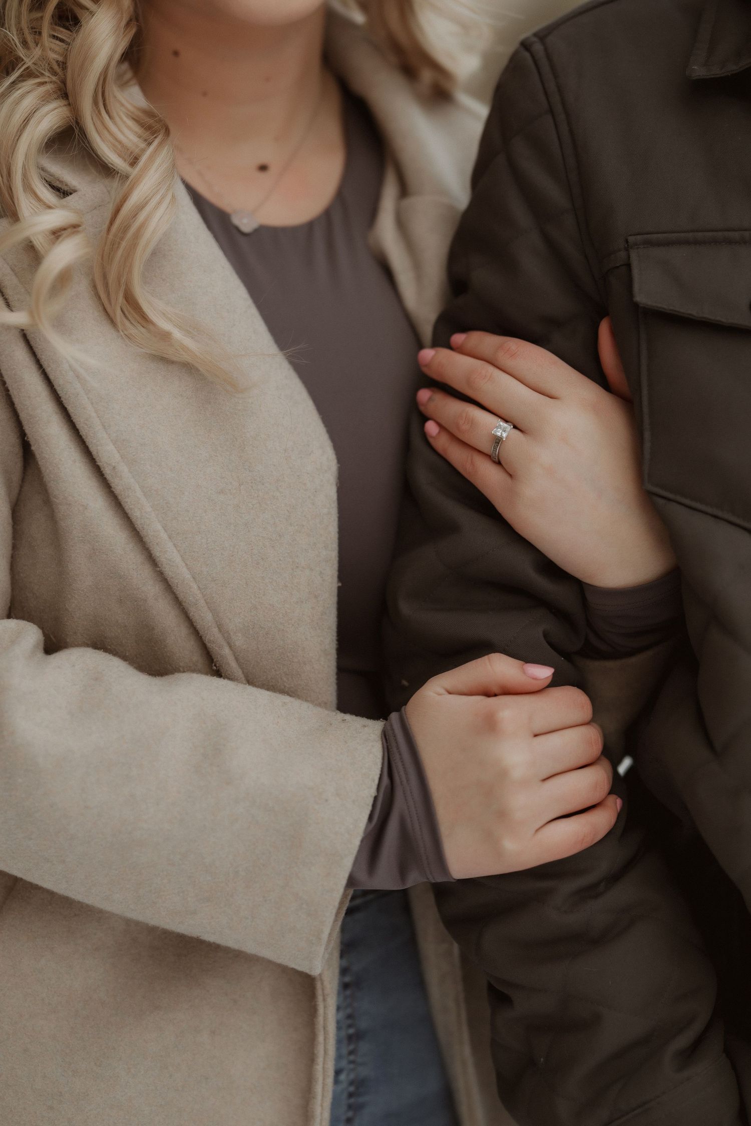 Close-up shot showing hands with engagement ring and cozy winter outerwear.