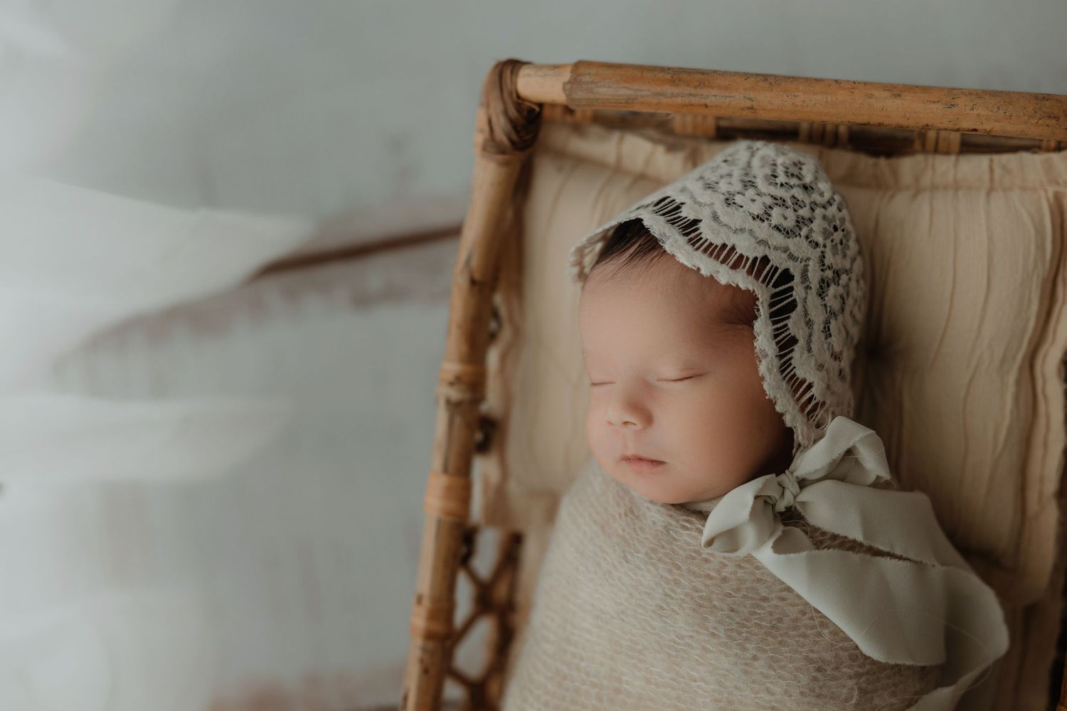 Sleeping infant wearing vintage-style lace bonnet in wooden prop.