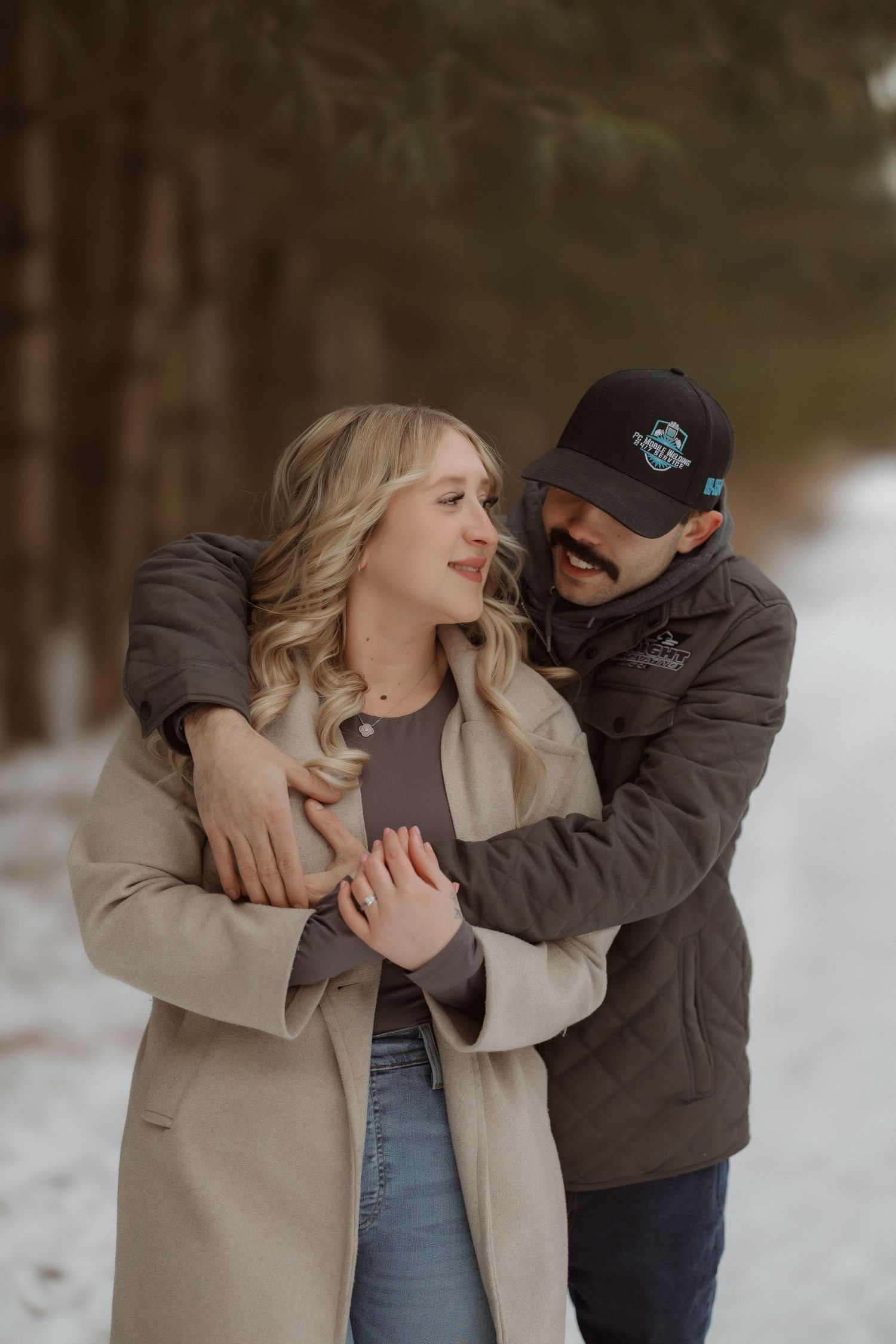 A joyful winter engagement photo with the couple laughing together in the snow.