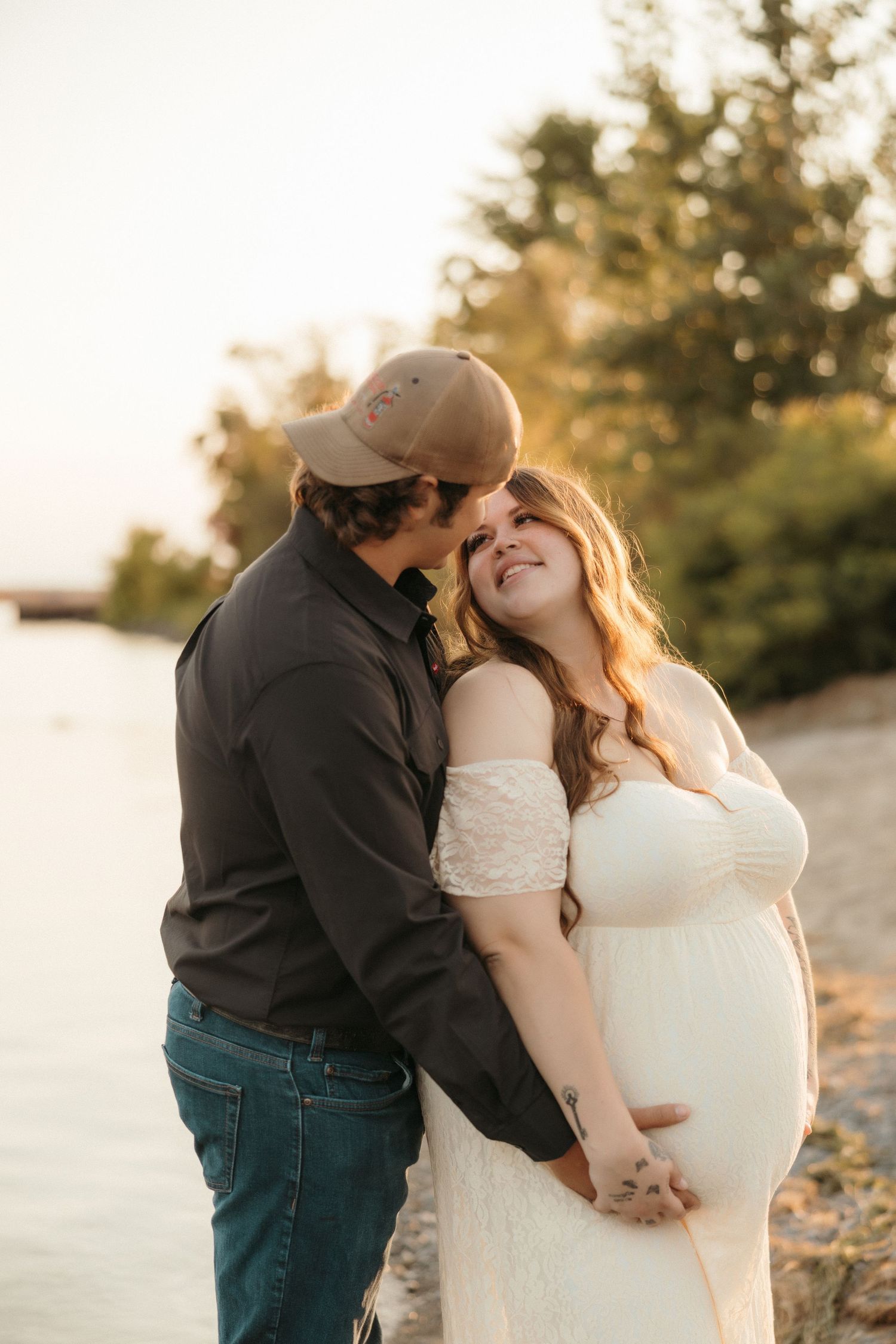 Romantic sunset maternity photo of couple embracing on beach.